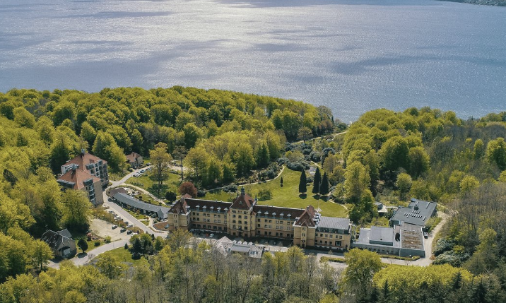Sunset over a historic castle next to a river with trees and a bridge in the background.