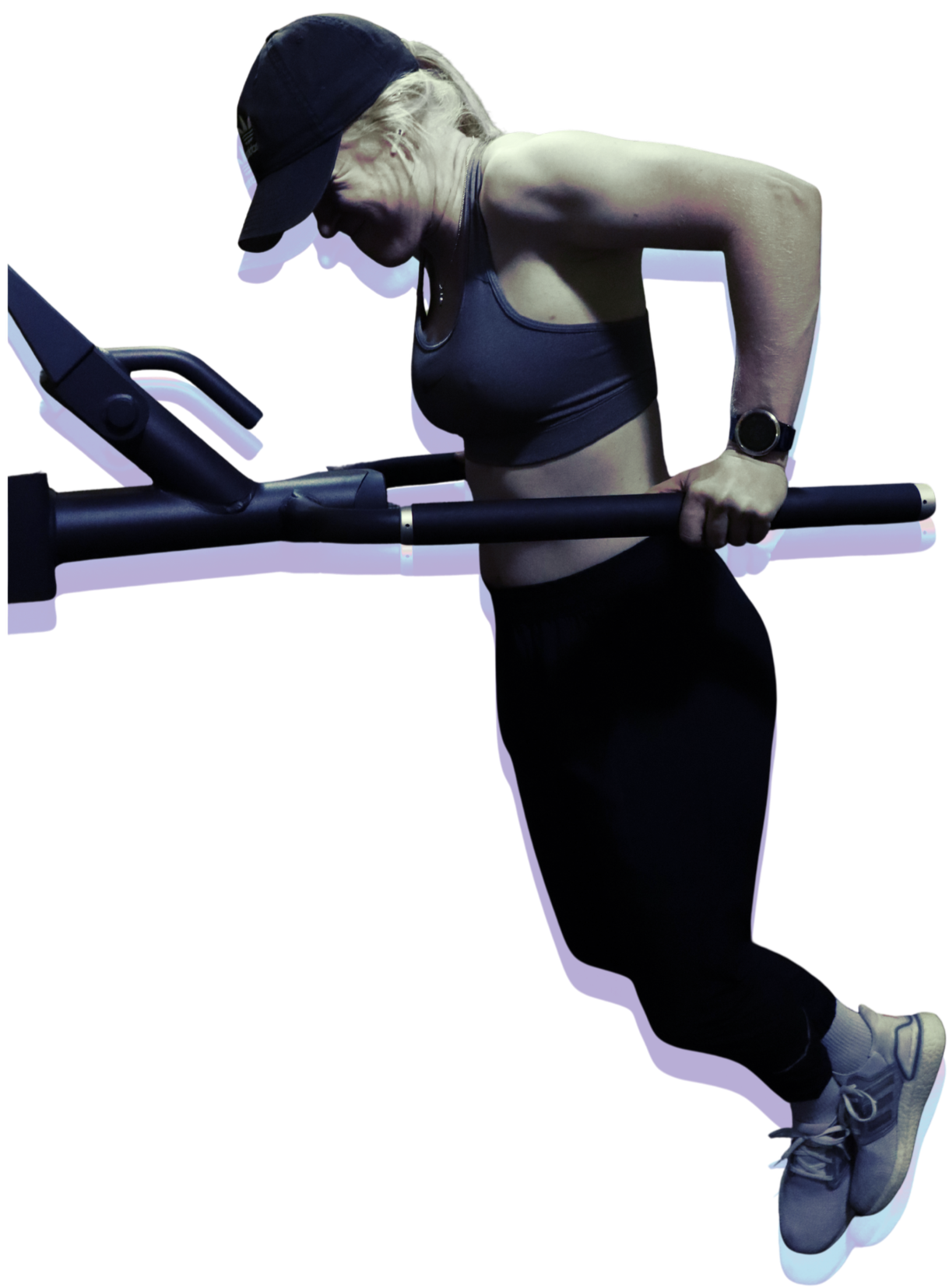 A woman in athletic wear, including a cap, sports bra, and leggings, using a rowing machine in a dimly lit environment.