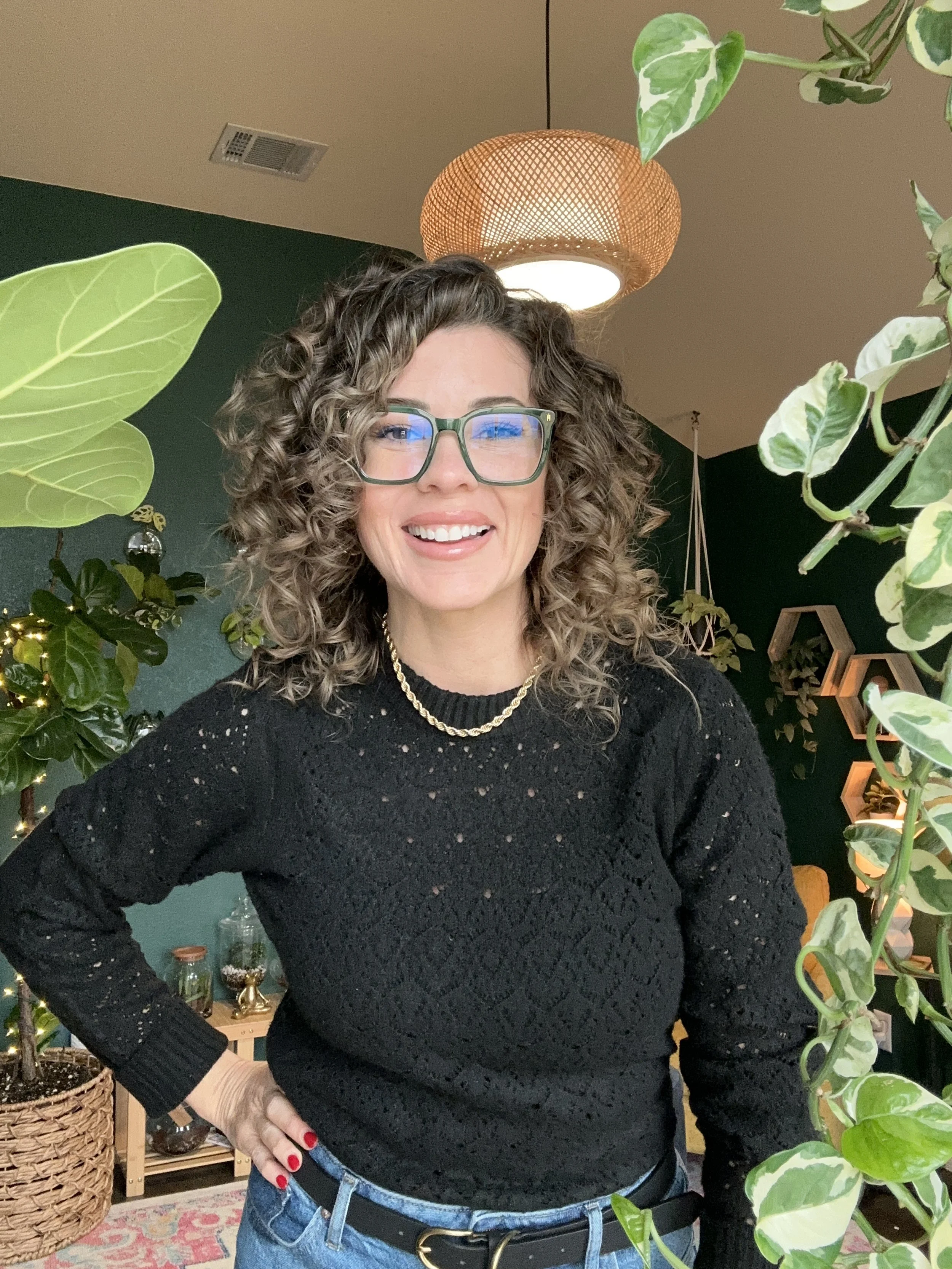 Lauren White smiling in her plant studio, wearing glasses and a black shirt with indoor plants in the background.