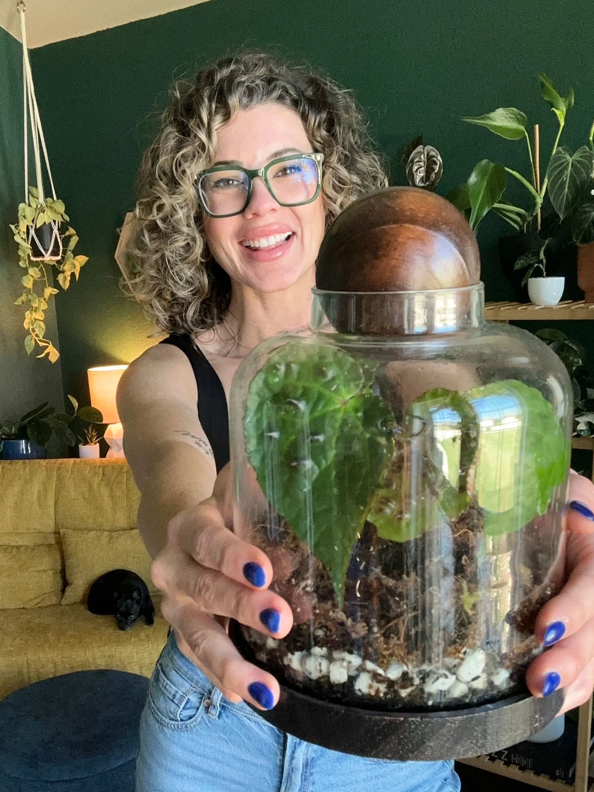 Lauren smiling while holding a terrarium with a begonia ferox inside in her plant room in Fort Worth, Tx.