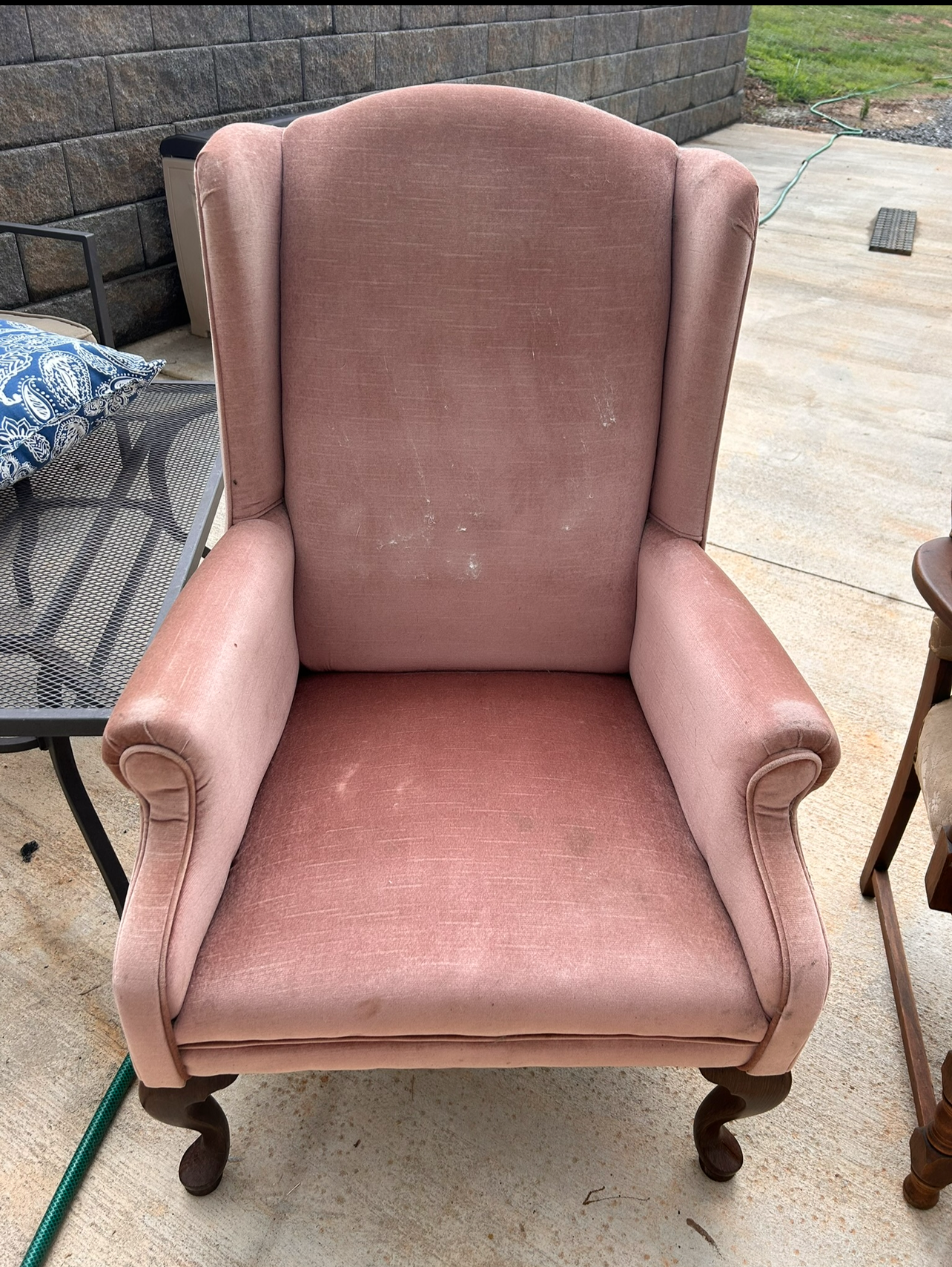 Before reupholstery: Vintage wingback chair with faded rose upholstery, rolled arms, and curved wooden legs.
