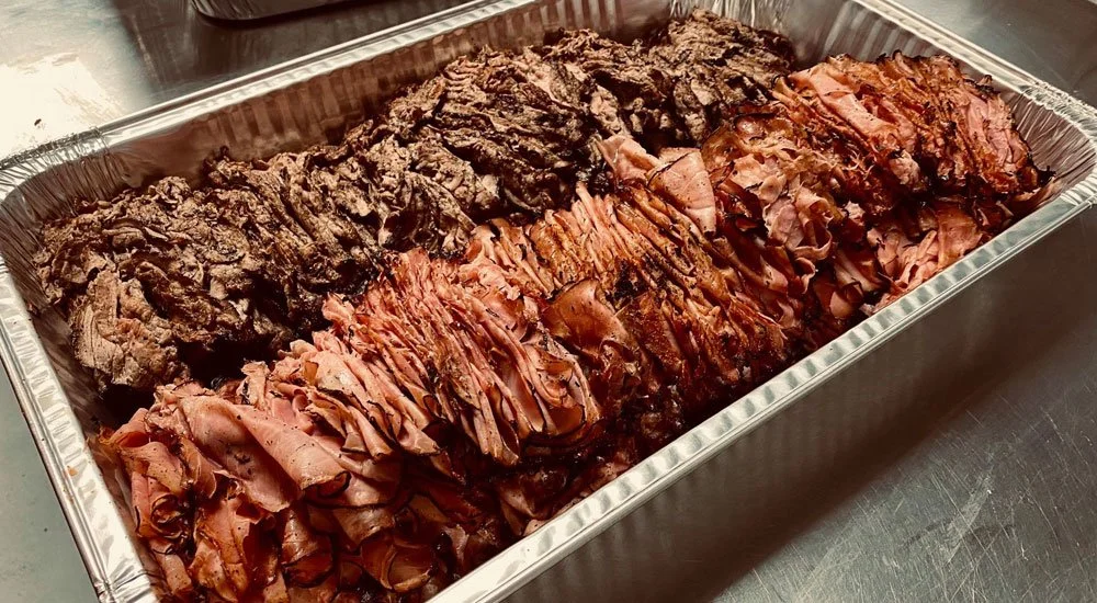 Aluminum tray containing sliced roast beef and cooked steak.