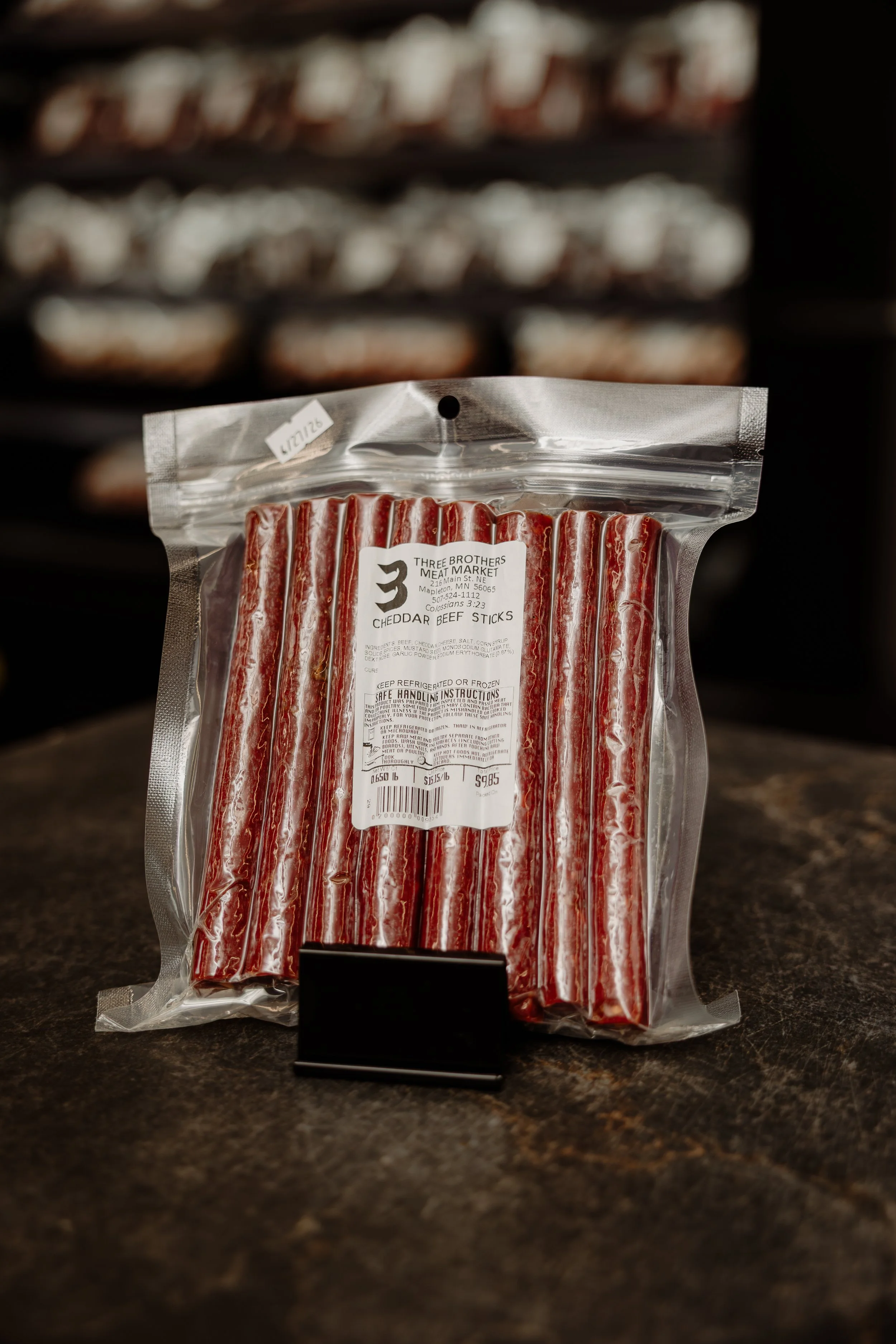 A package of cheddar beef sticks on a countertop with a blurred background of refrigerated shelves.