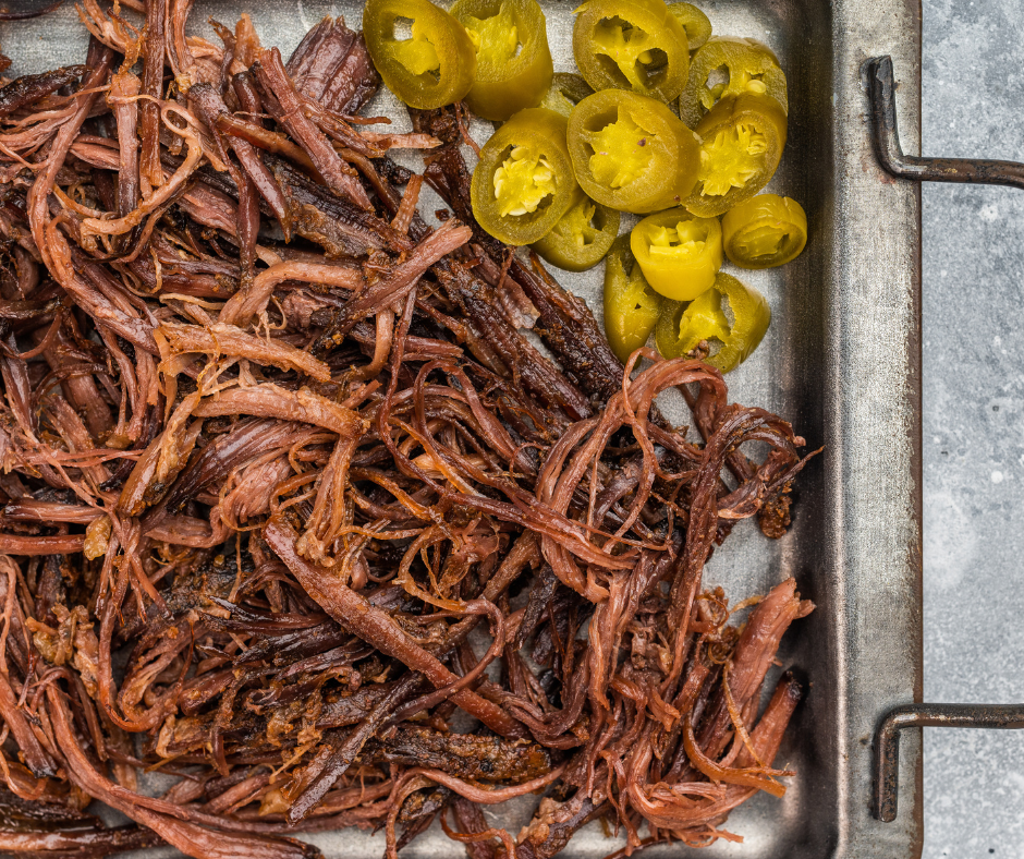 Shredded cooked beef with sliced jalapeños on a metal tray.
