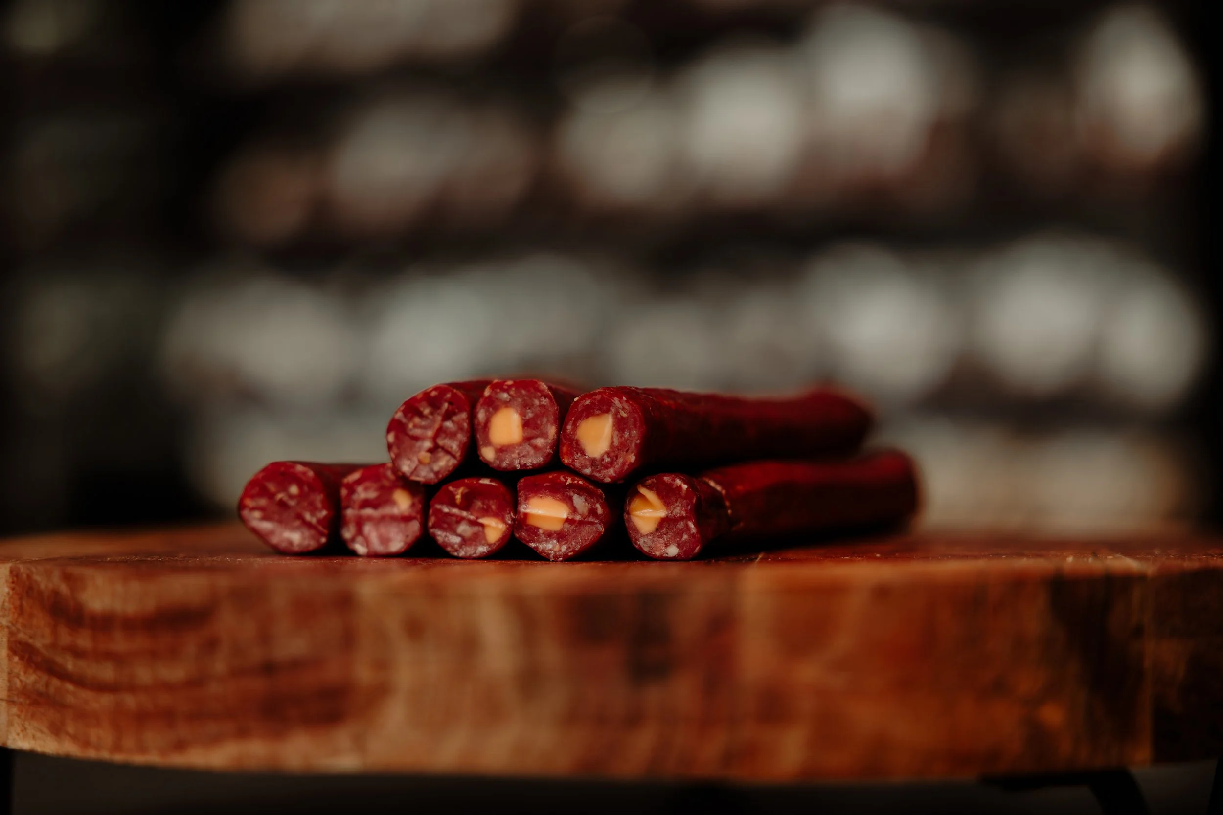 Close-up of several slices of red sausage with cheese, stacked on a wooden surface, with blurred background.