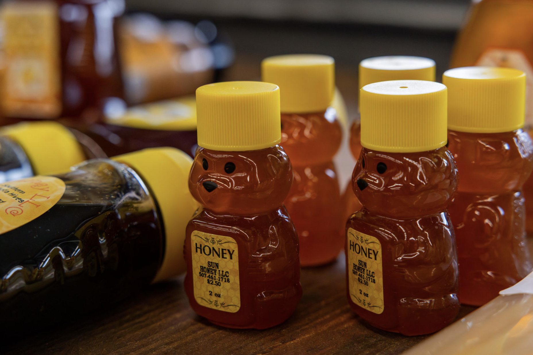 Small bear-shaped bottles of honey with yellow caps on a wooden surface.