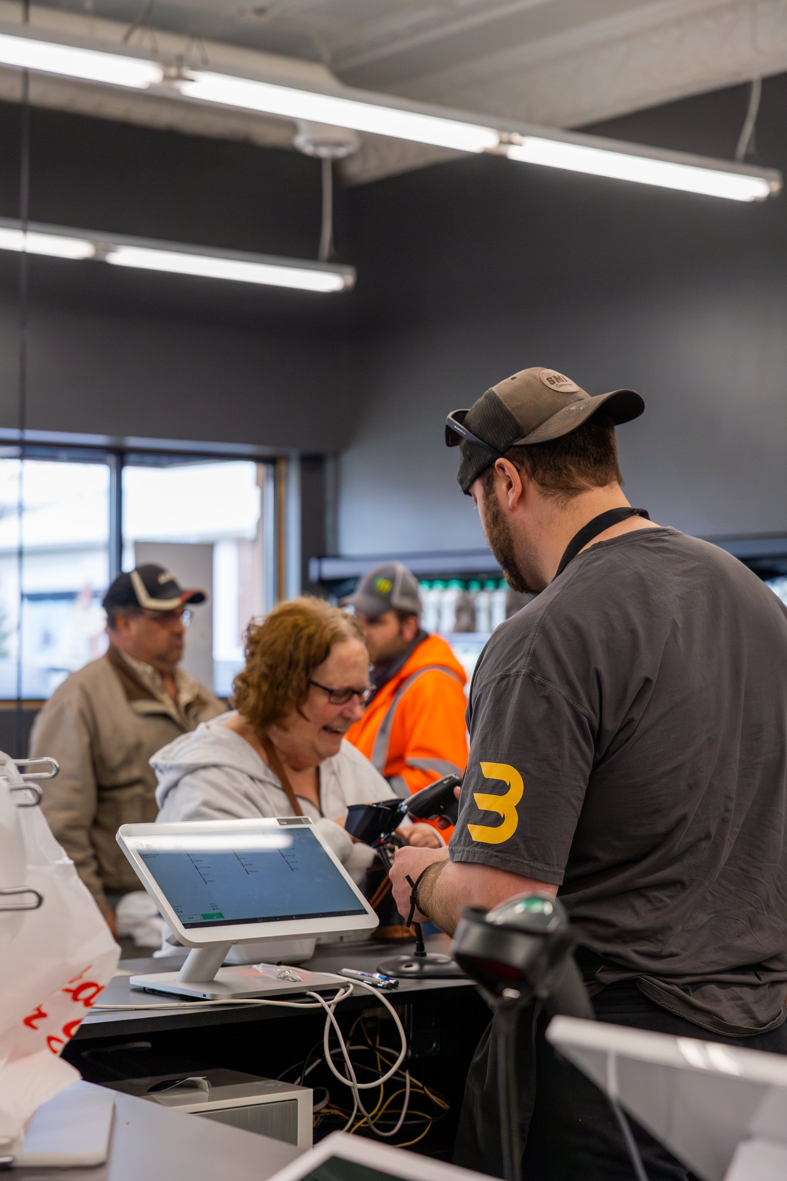 Customer at a checkout counter smiling and interacting with a cashier in a retail store, with other shoppers in the background.