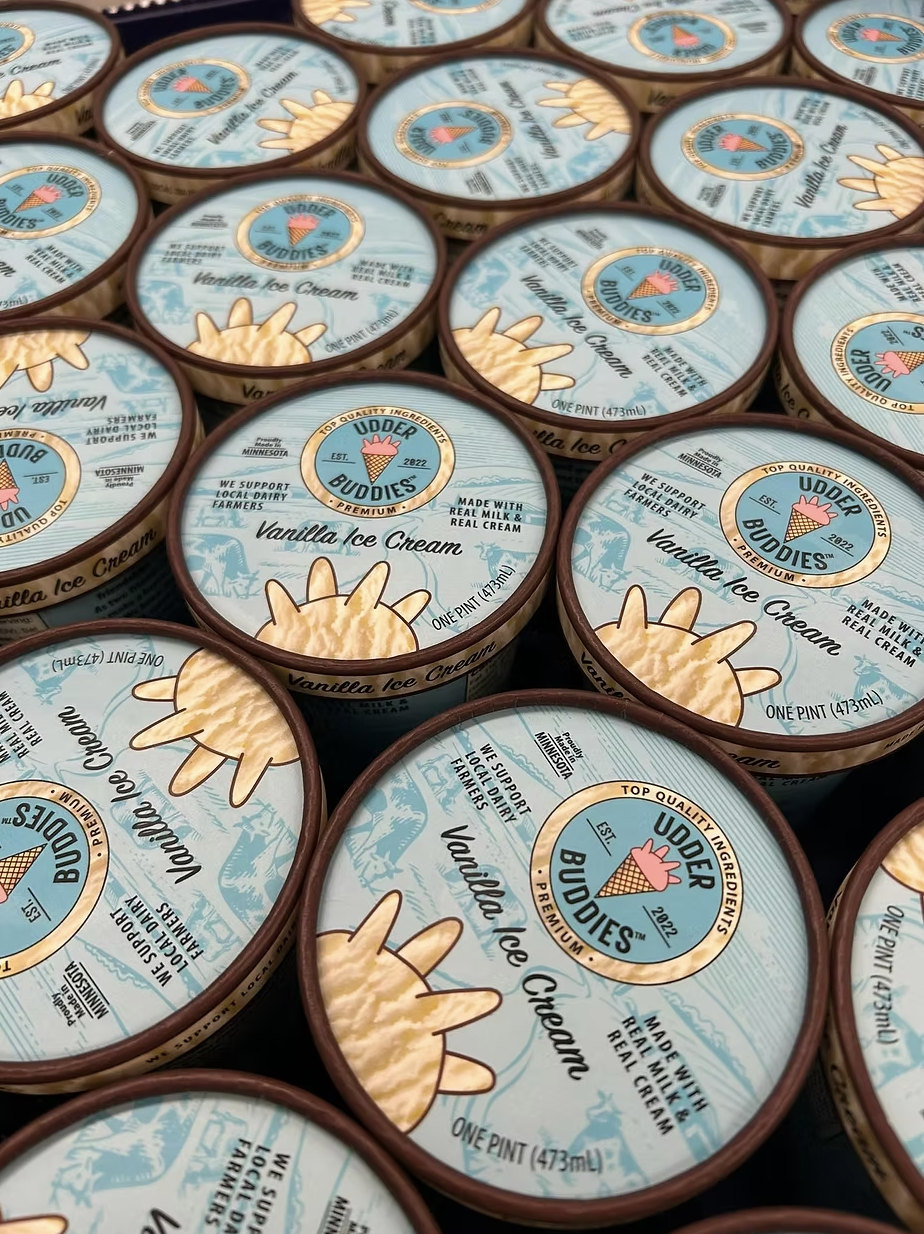 Multiple containers of Udder Buddies Vanilla Ice Cream with cartoon cow branding, supporting local dairy farmers in Minnesota.