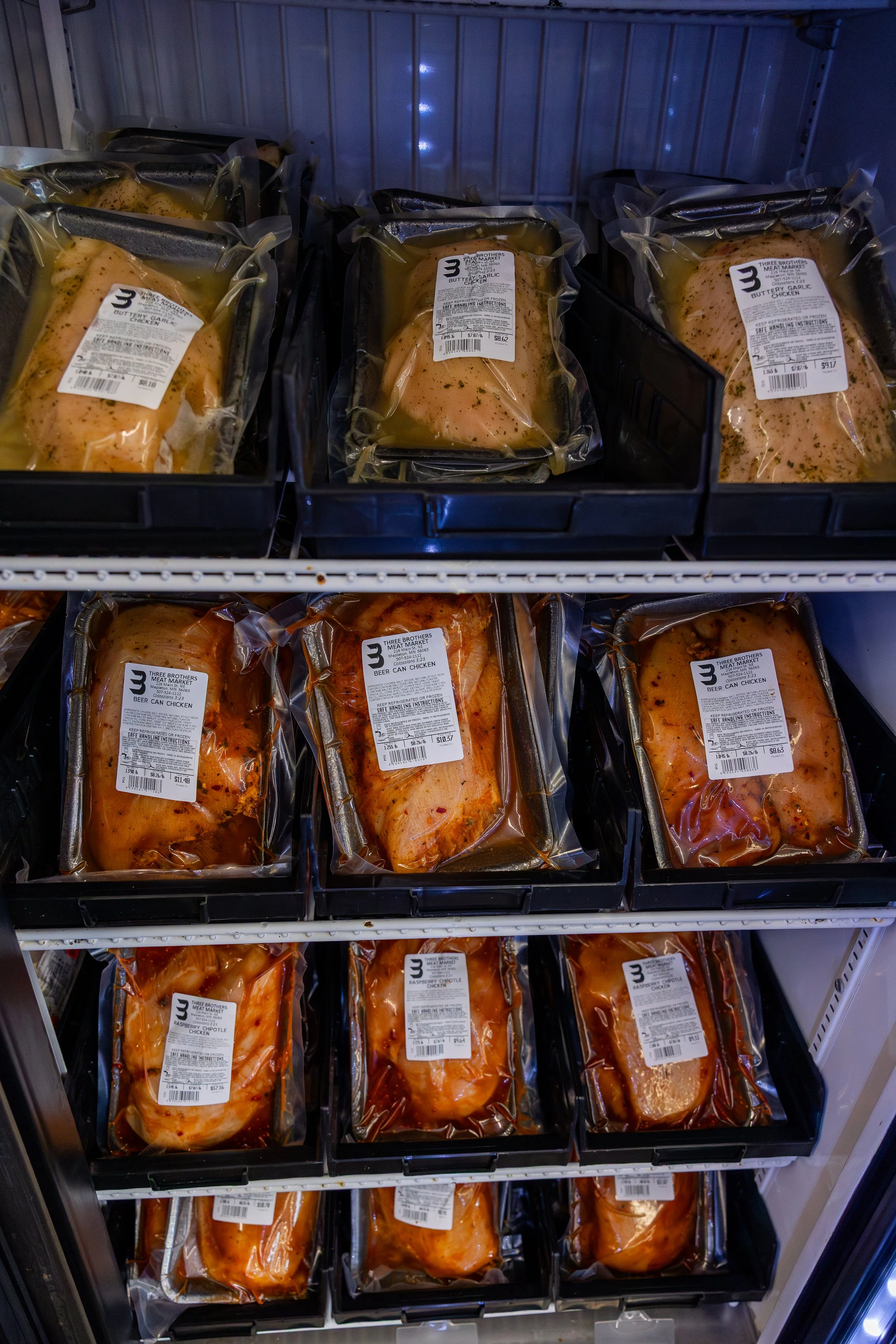 Multiple packages of marinated chicken breasts and drumsticks in vacuum-sealed plastic, stored on refrigerated shelves in a grocery store.