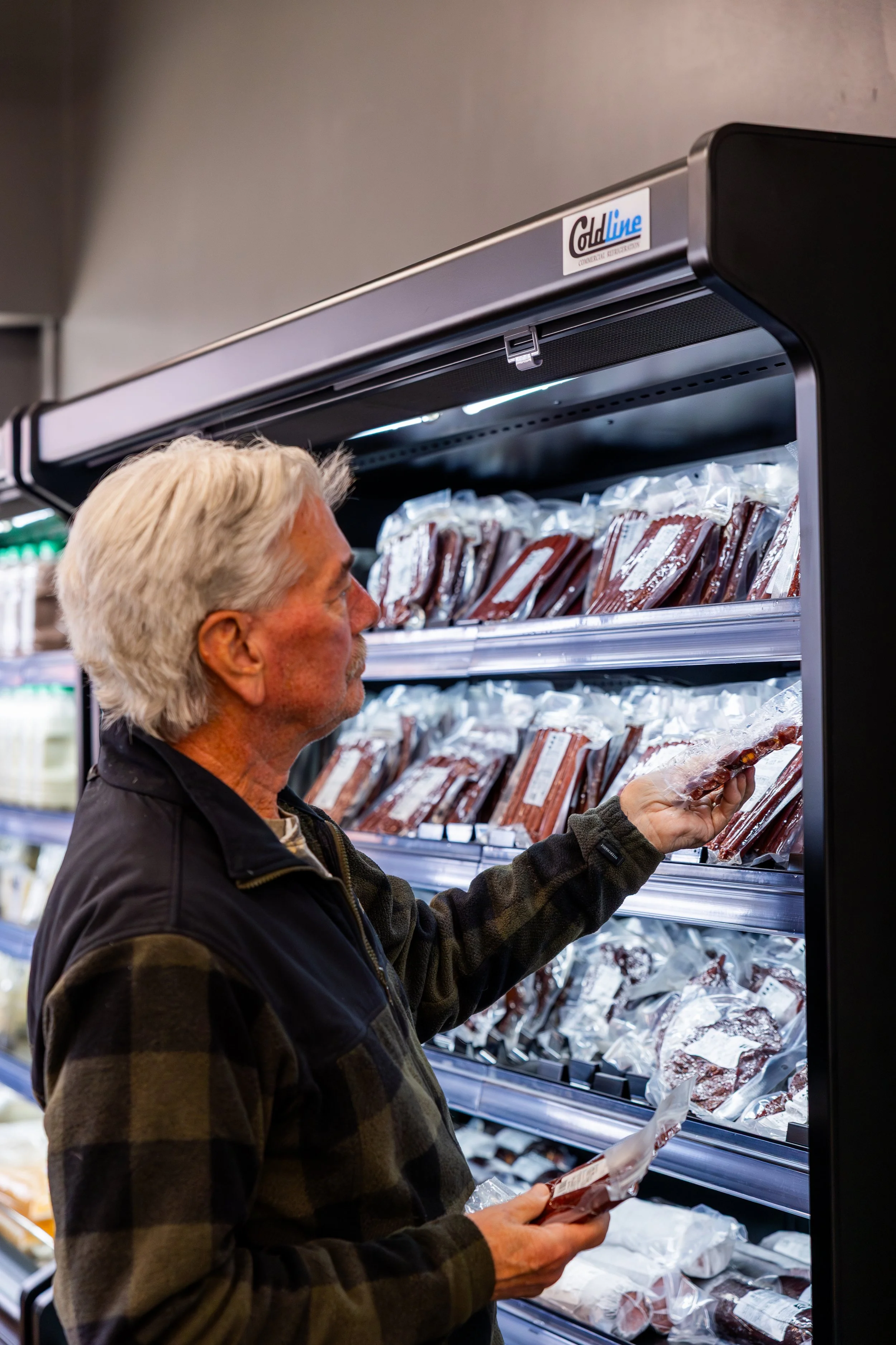 A man shopping in the refrigerated section of a grocery store, selecting packaged meat.