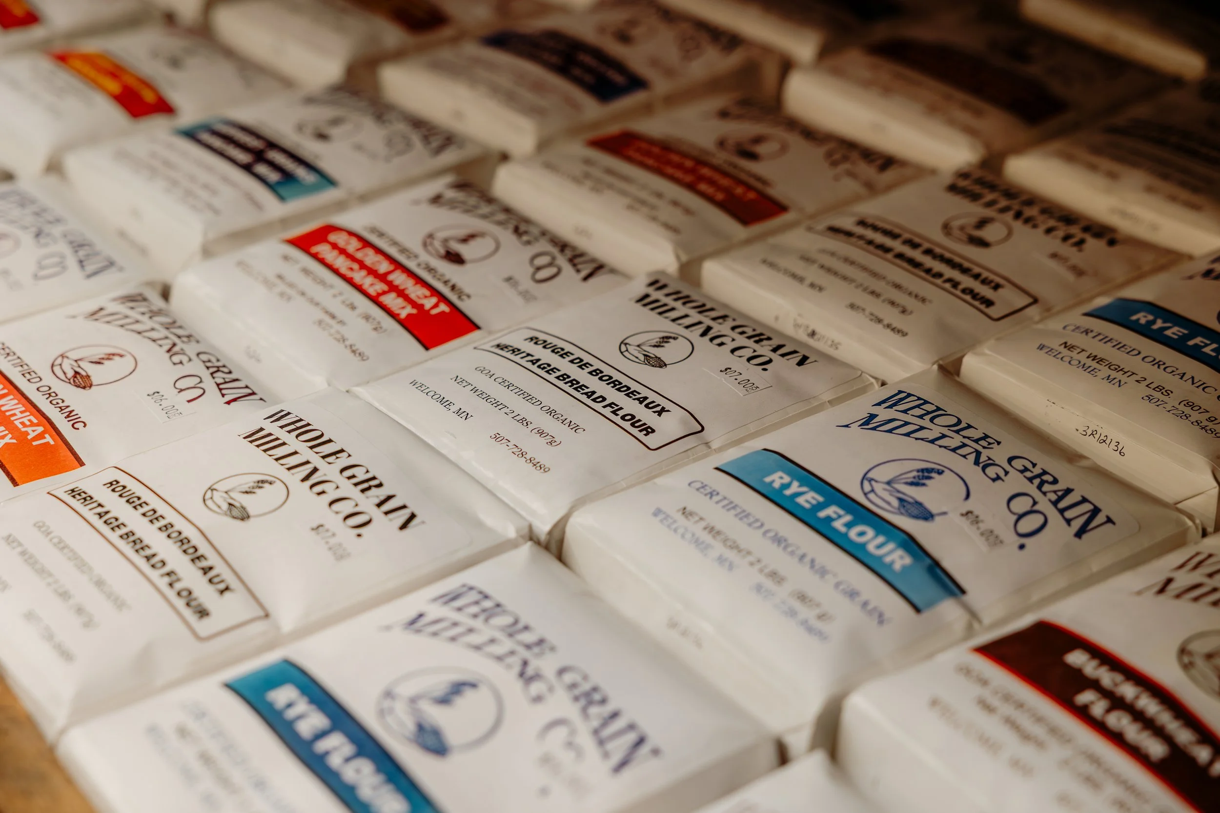 Several packages of Whole Grain Milling Co. rye bread flour, featuring white packaging with blue, red, and black labels, laid out on a flat surface.