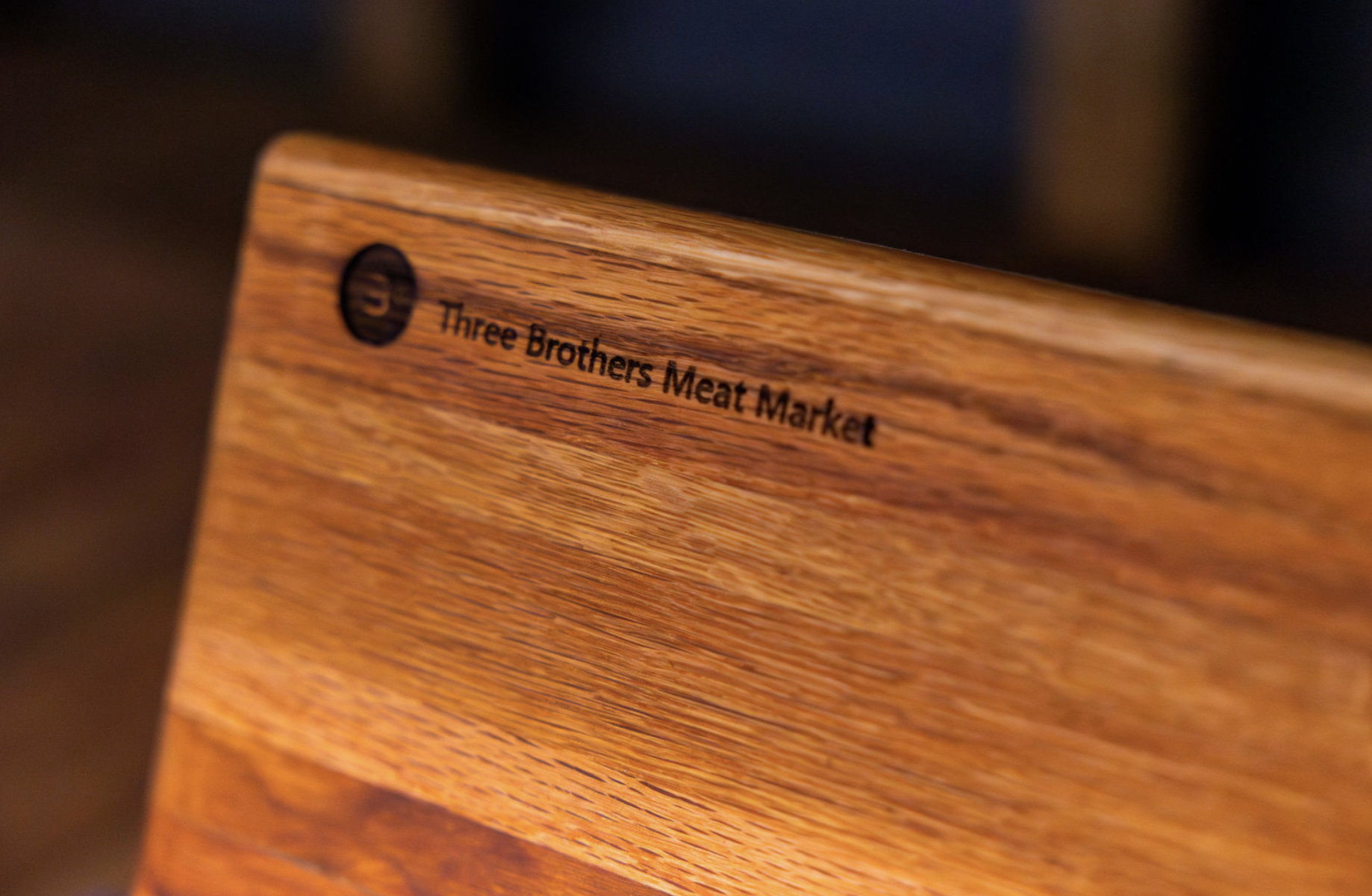 Close-up of a wooden board with the logo and text 'Three Brothers Meat Market' printed on it.