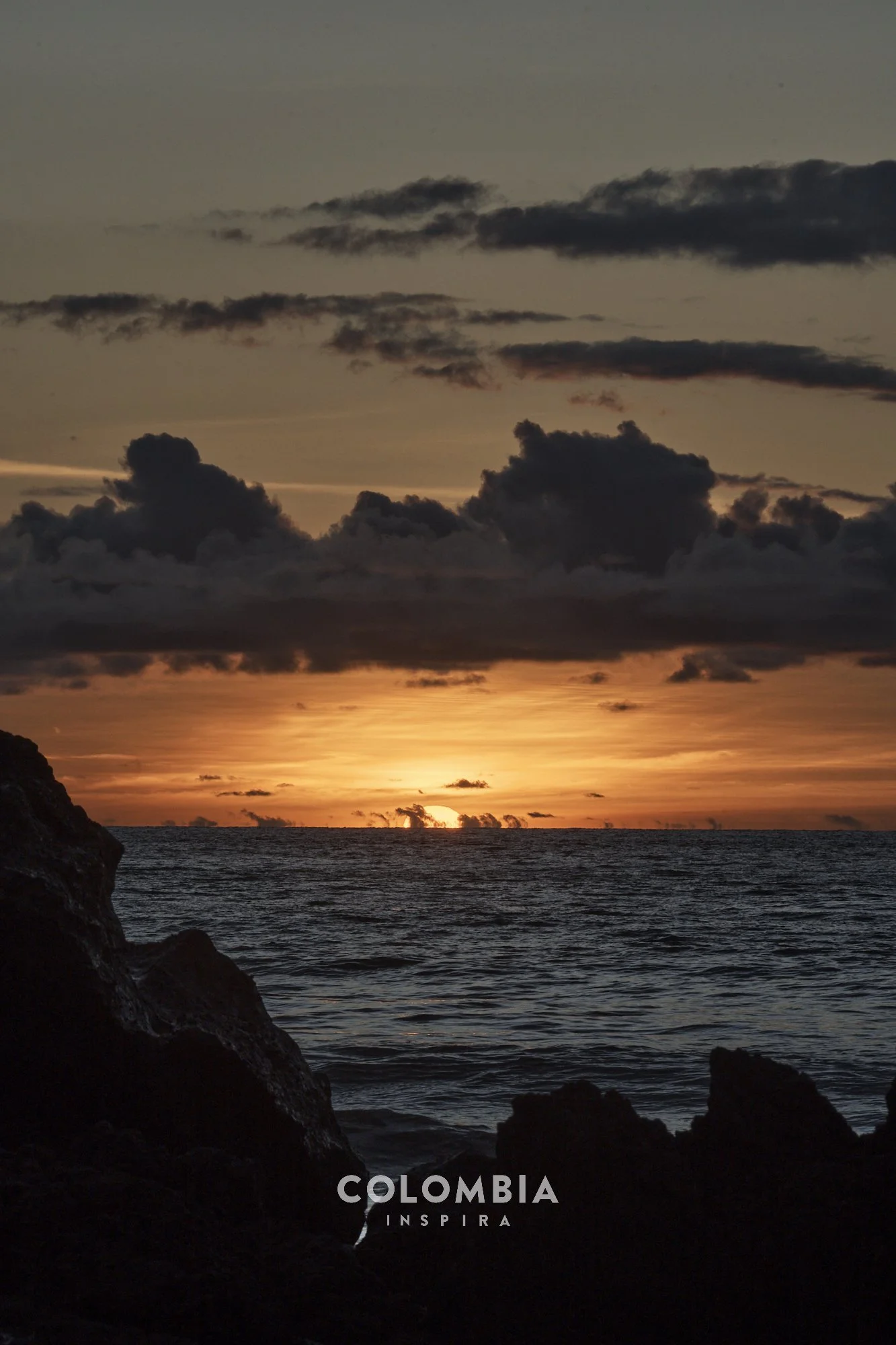 Sunset over the ocean with dark clouds and rocky shoreline in Colombia.