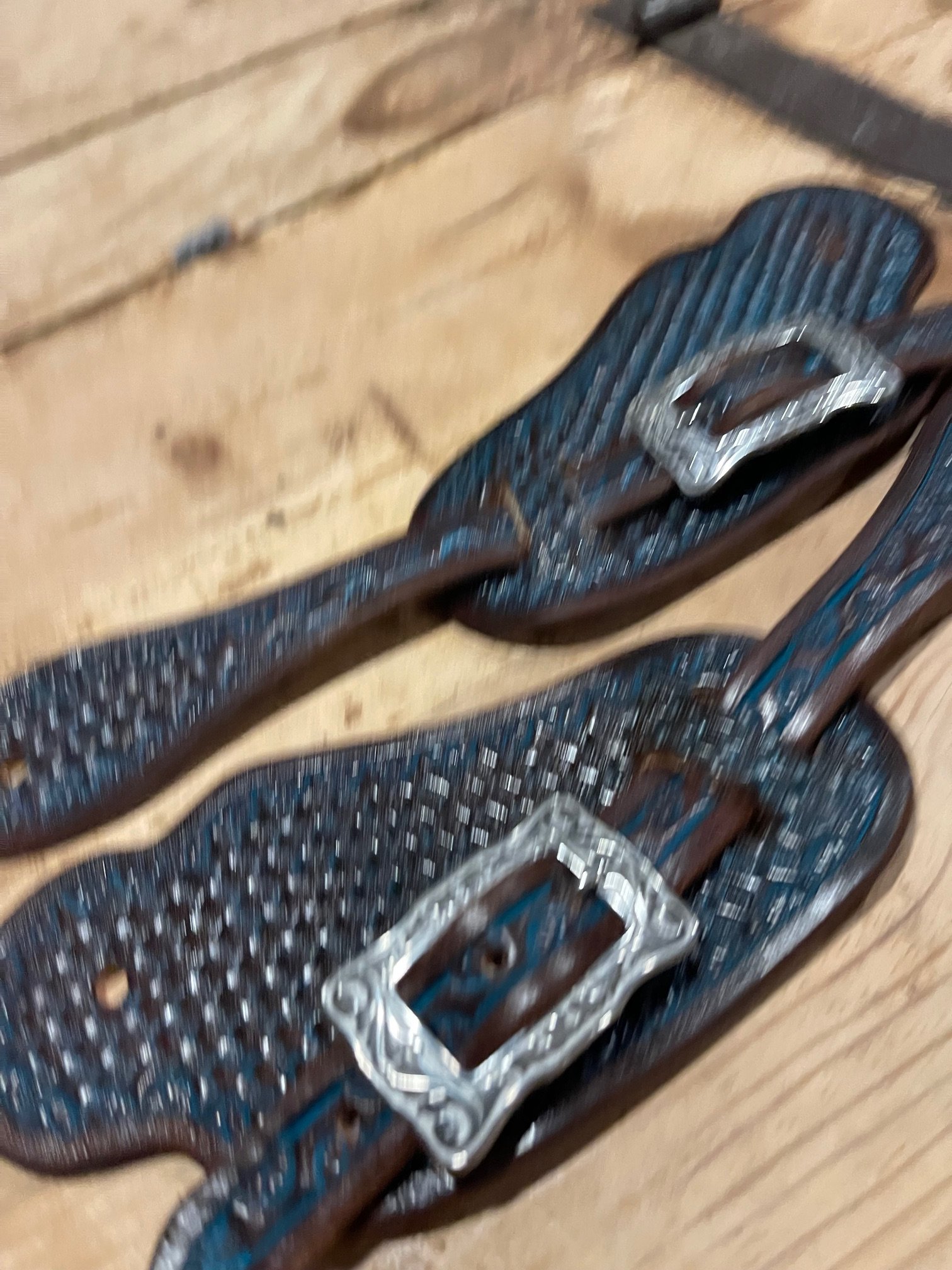 Close-up of a pair of dark brown men's belt buckles with silver accents, lying on a wooden surface.