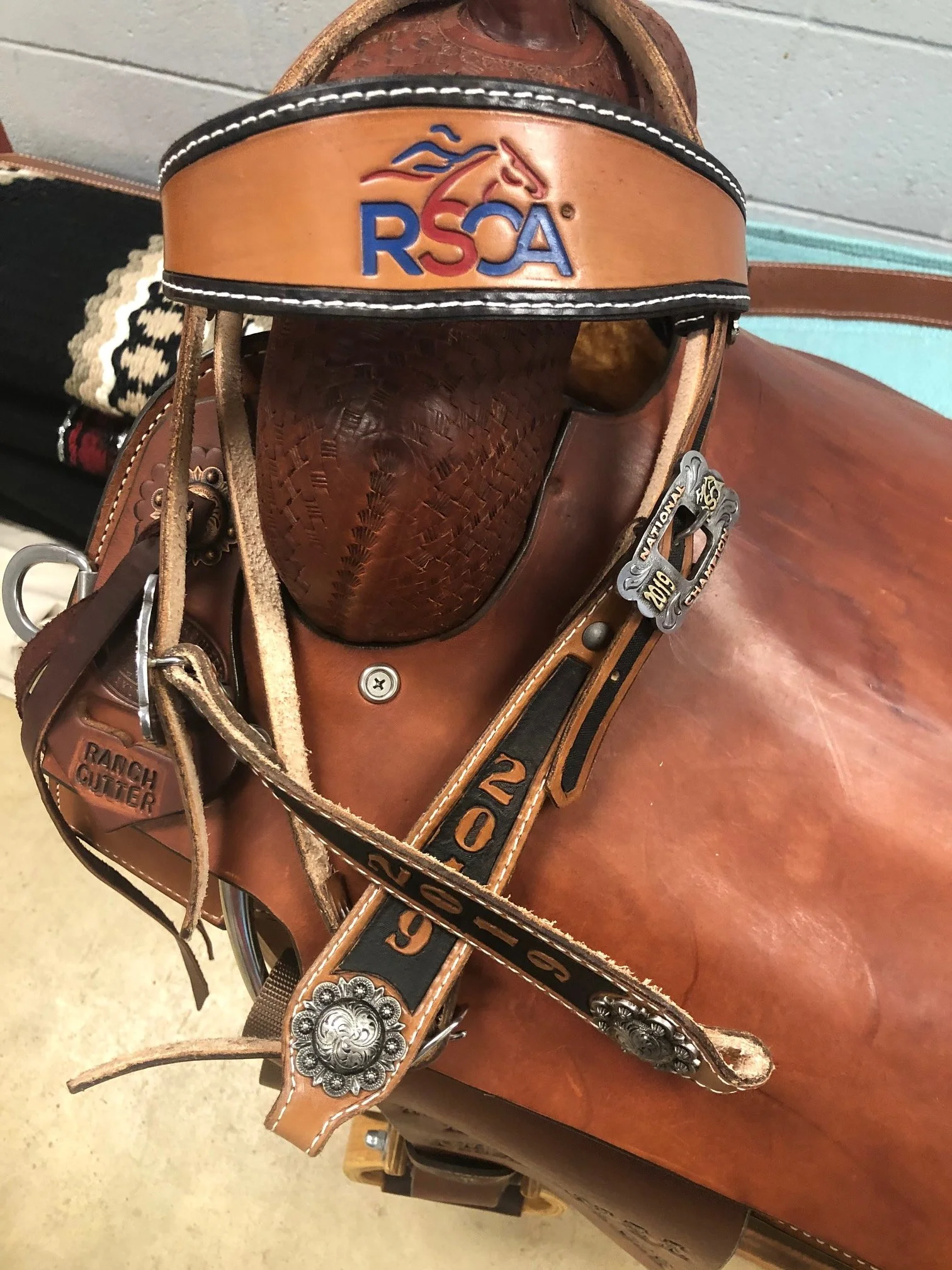 custom bridle with leather straps, silver decorative conchos, and a saddle horn, placed on a wooden surface.