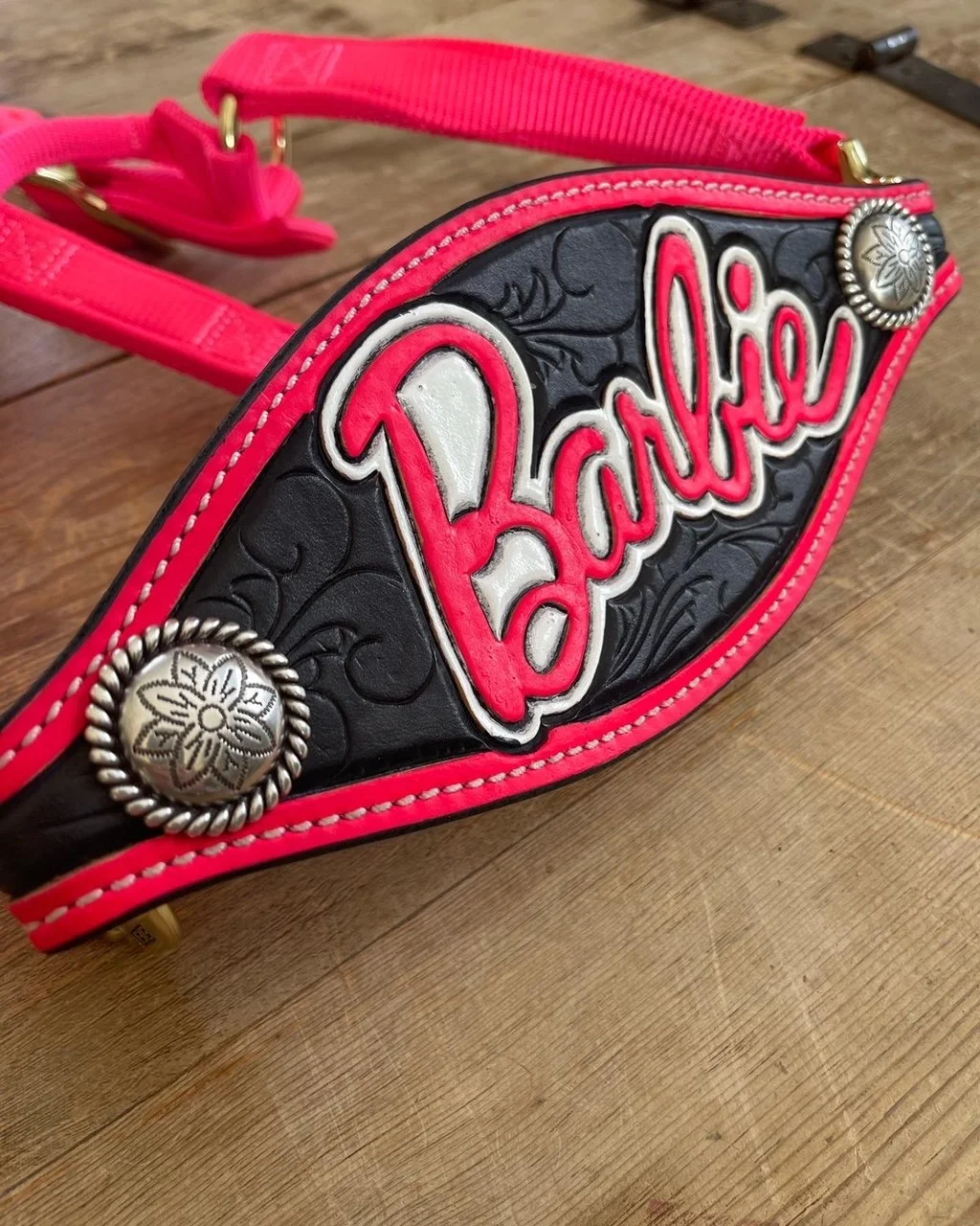 Close-up of a colorful Barbie-themed bronc halter with pink and black details, decorative stitching, and metal embellishments, placed on a wooden surface.