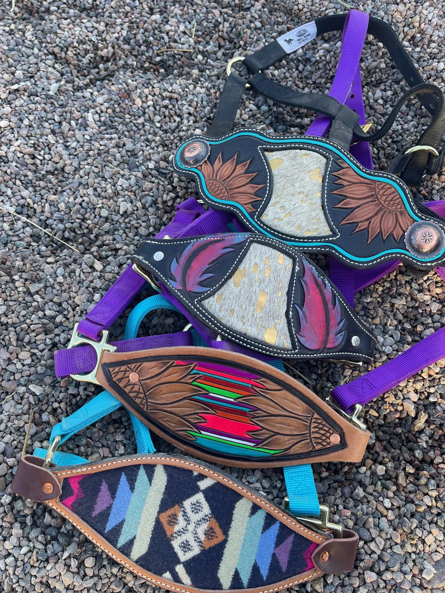 Four colorful and decorative bronc halters with various patterns and designs, lying on gravel ground.