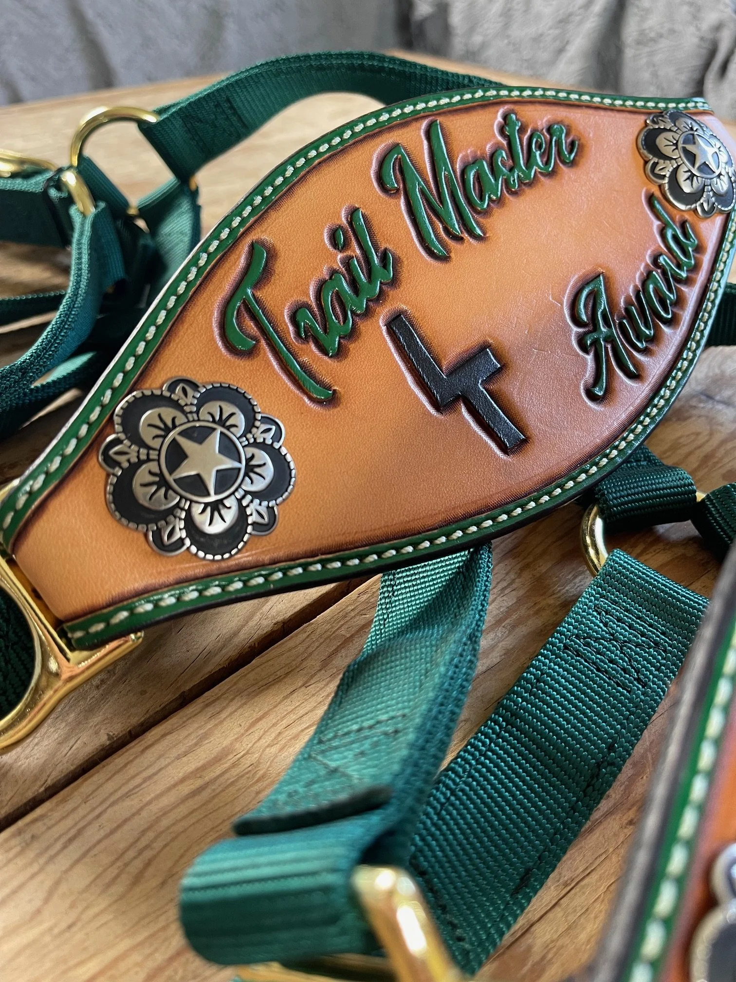 A leather bronc halter with green embroidery that says 'Thank Mother' and 'Funday,' with a black cross in the middle and decorative metal flower-shaped embellishments.