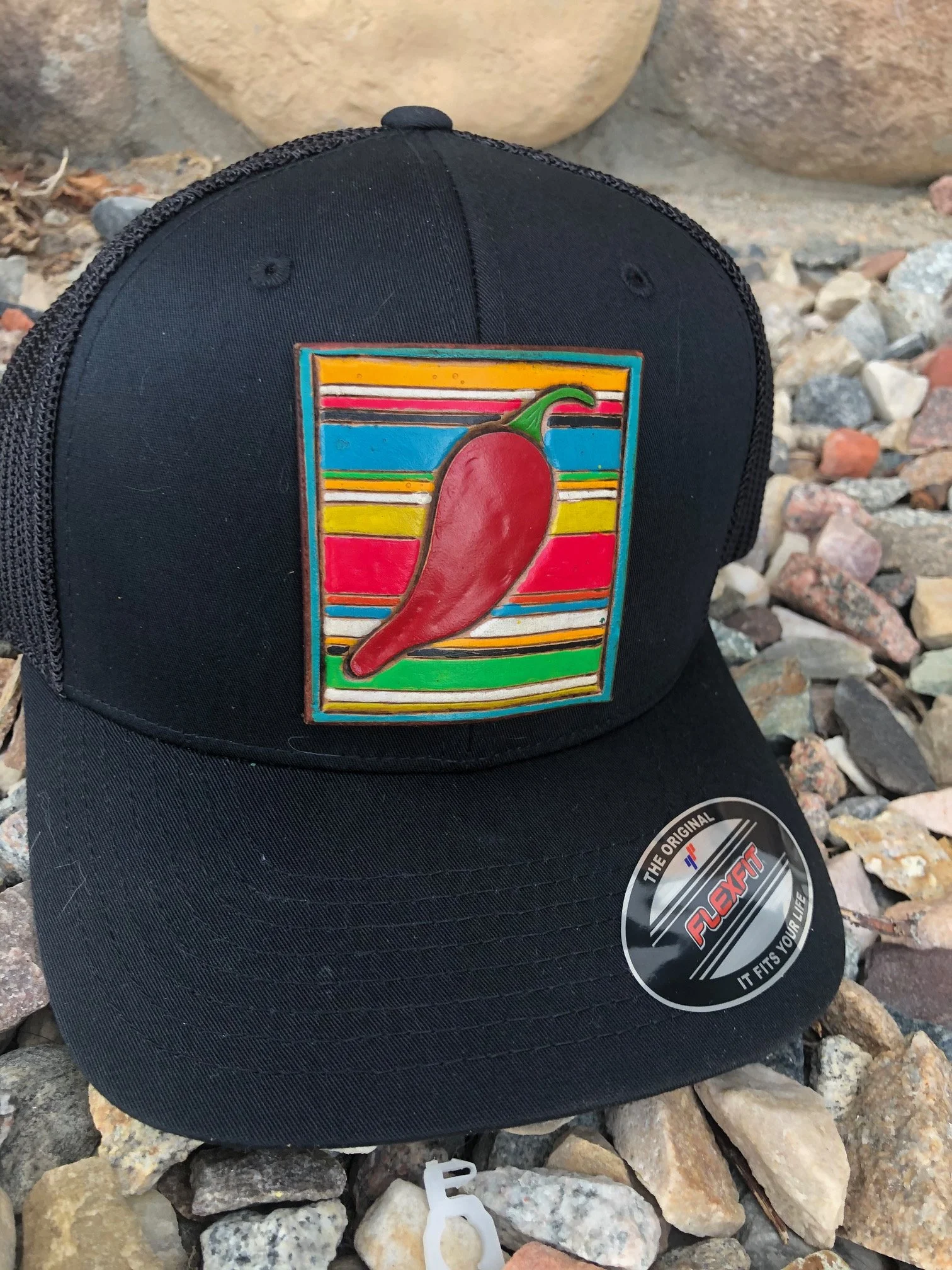 Black baseball cap with a colorful patch of a chili pepper and striped background.
