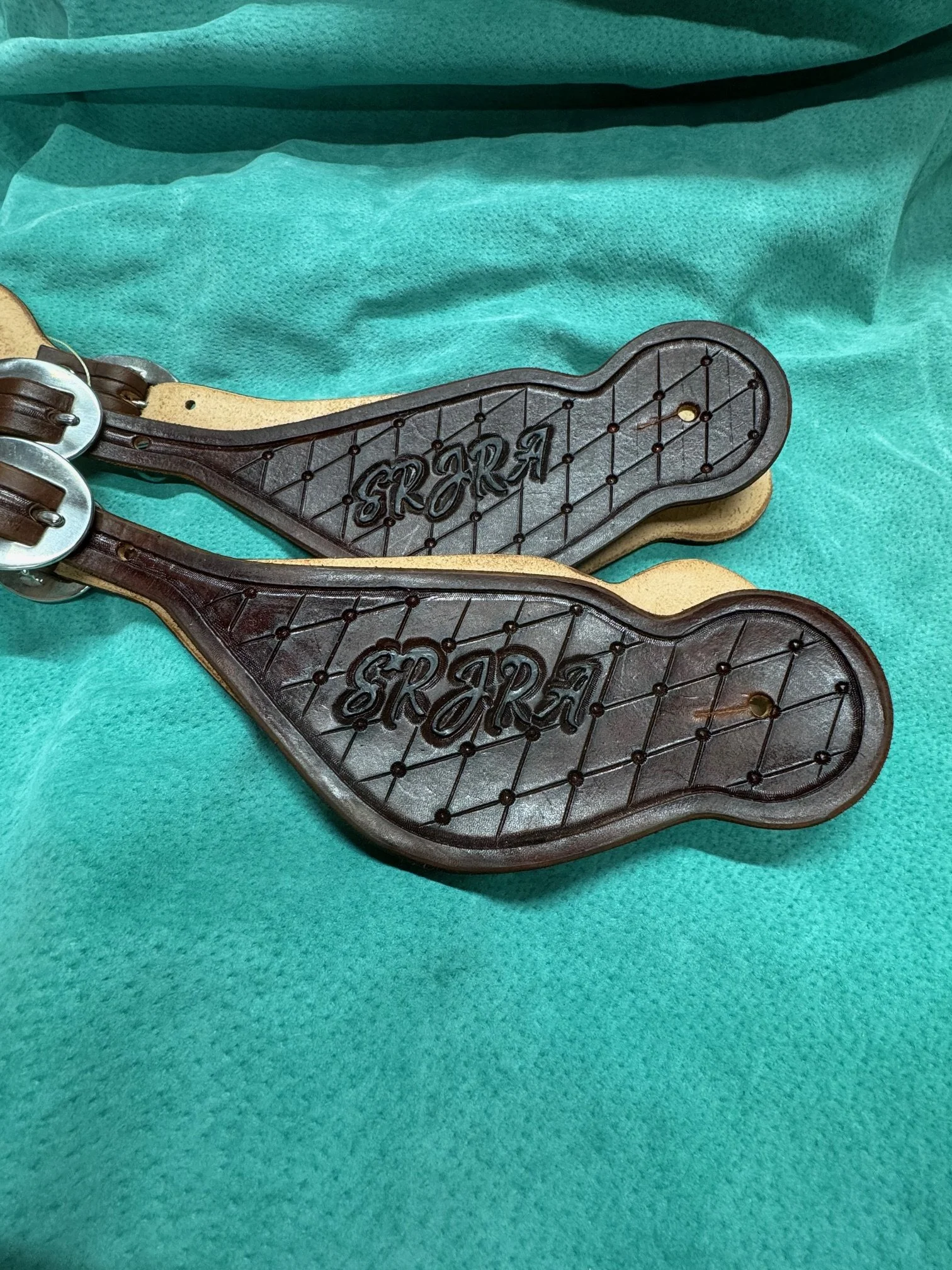 Two leather spur straps with the word 'STROF' embossed, resting on a teal medical drape.