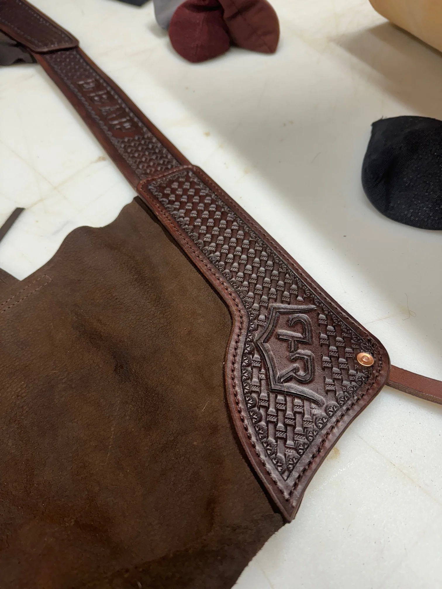 Close-up of a brown leather and suede bag with a woven leather strap, placed on a white surface with some socks nearby.