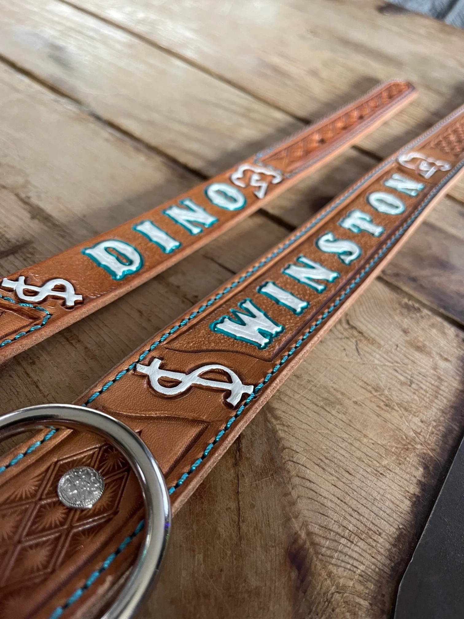 Leather dog collars with the words 'Won't Dog' embroidered in blue, adorned with silver dollar symbols, placed on a wooden surface.