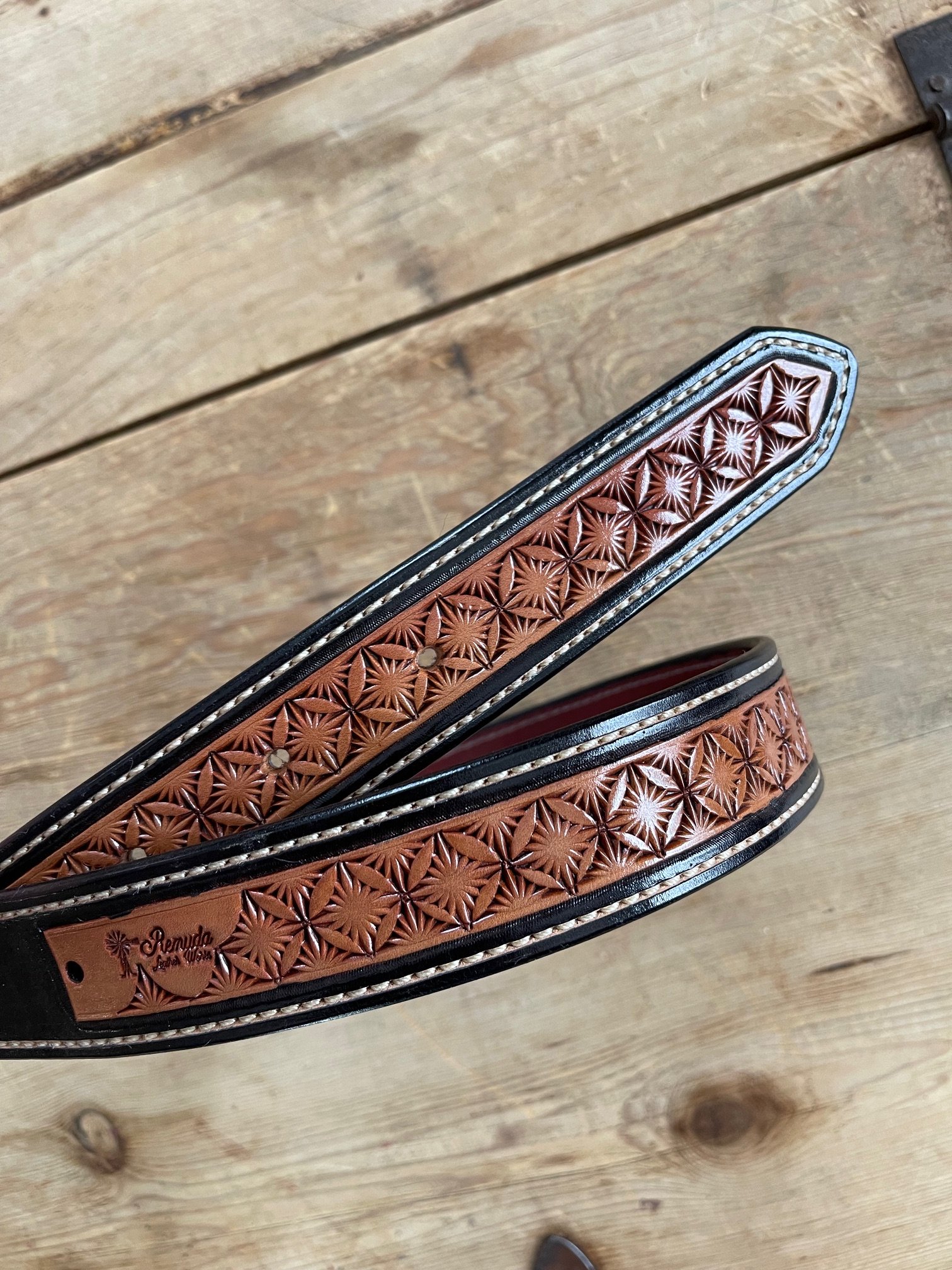 Close-up of a leather belt with intricate floral and geometric embossed patterns, placed on a wooden surface.