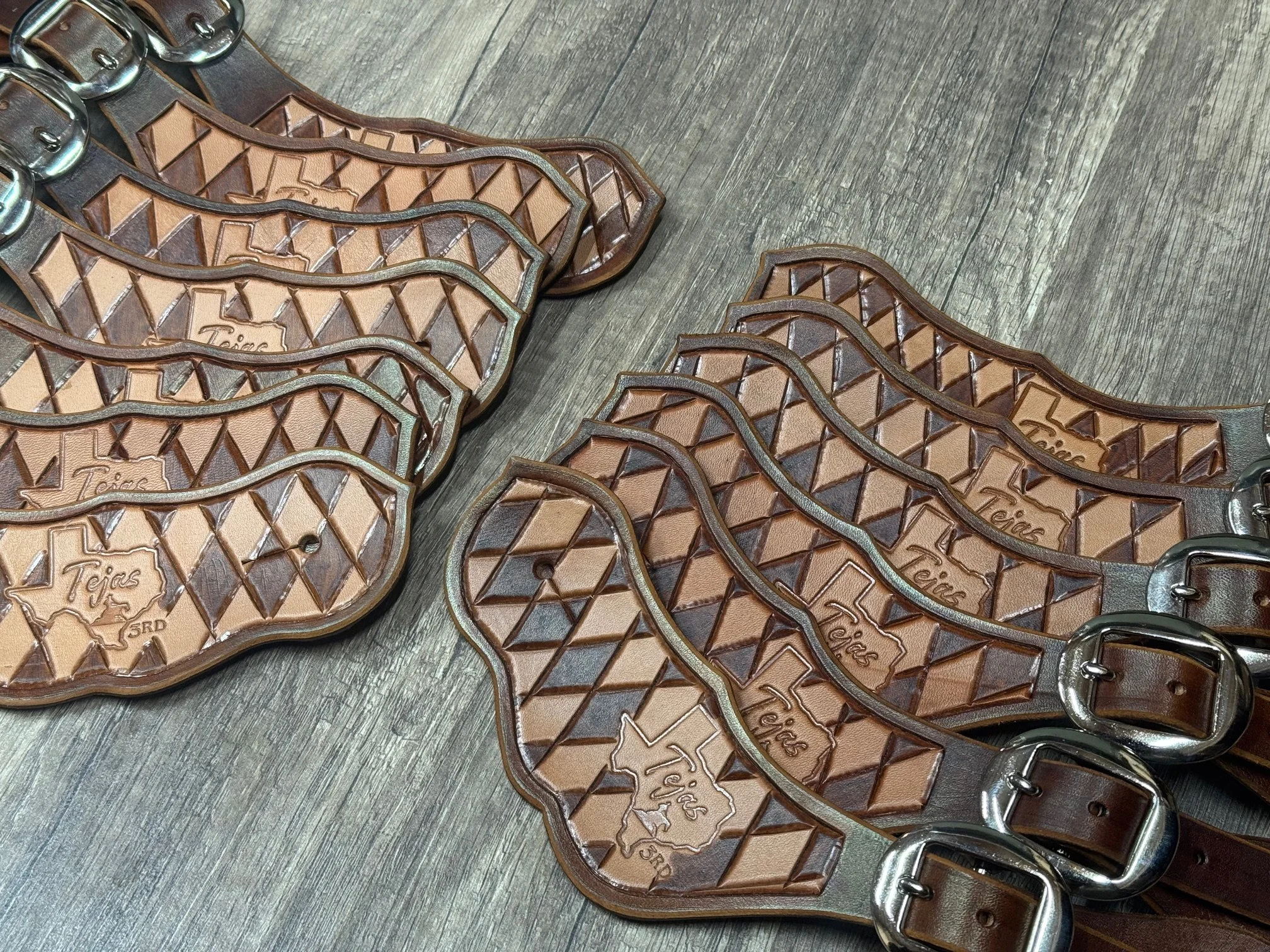 Leather belts with Texas map and diamond pattern, laid out on a wooden surface.