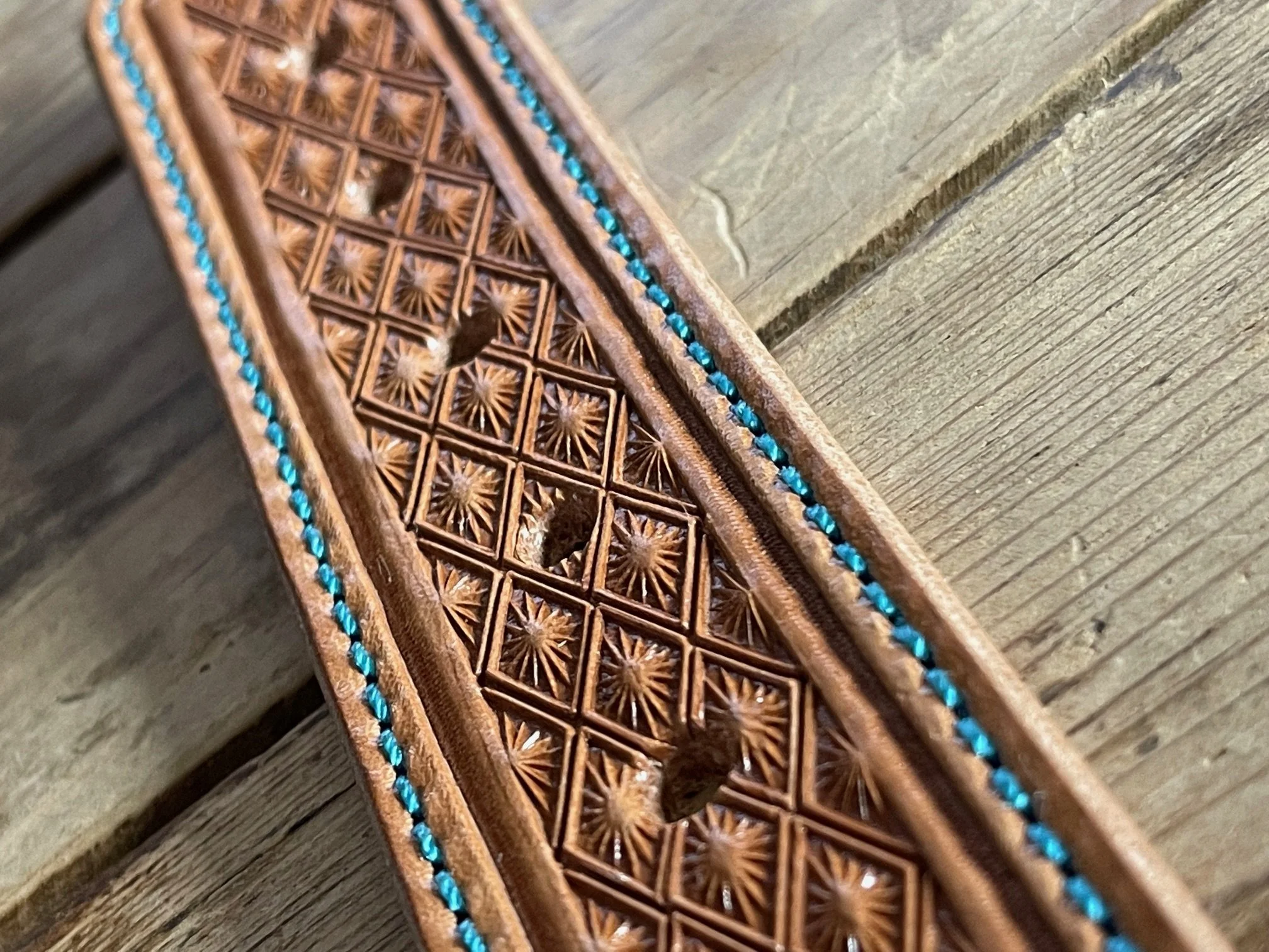 Close-up of a carved wooden object with intricate geometric patterns and blue inlays, placed on a wooden surface.