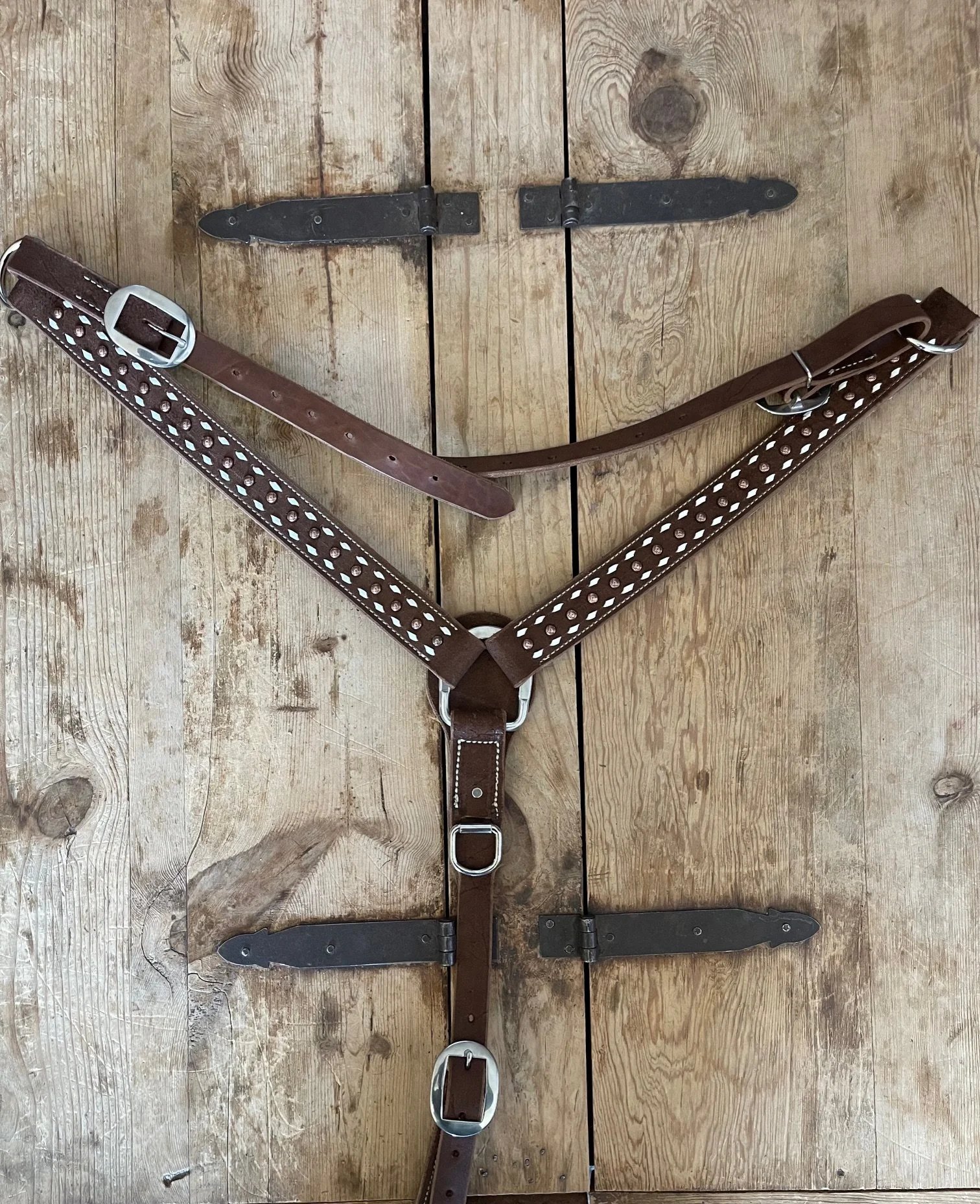A leather horse halter with metal buckles and adornments, laid flat on a wooden surface.