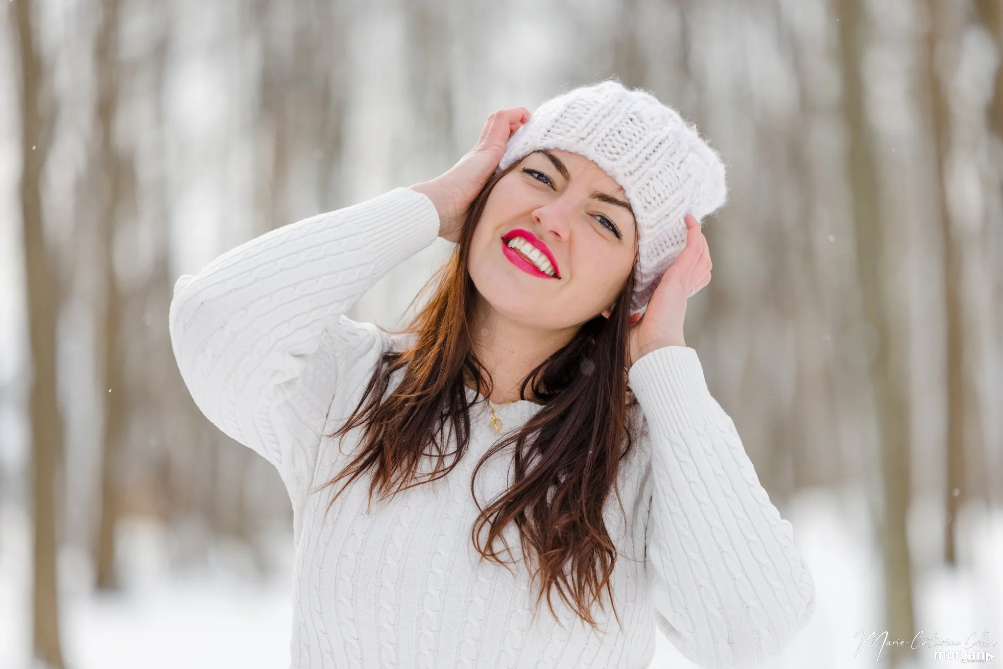 A woman smiling and holding her snow hat in a snowy forest during winter.