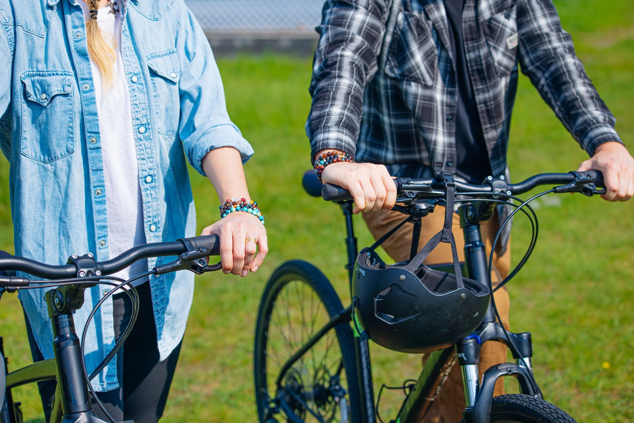 Two people with bicycles, one with a black helmet hanging on the bike, standing on a grassy area.