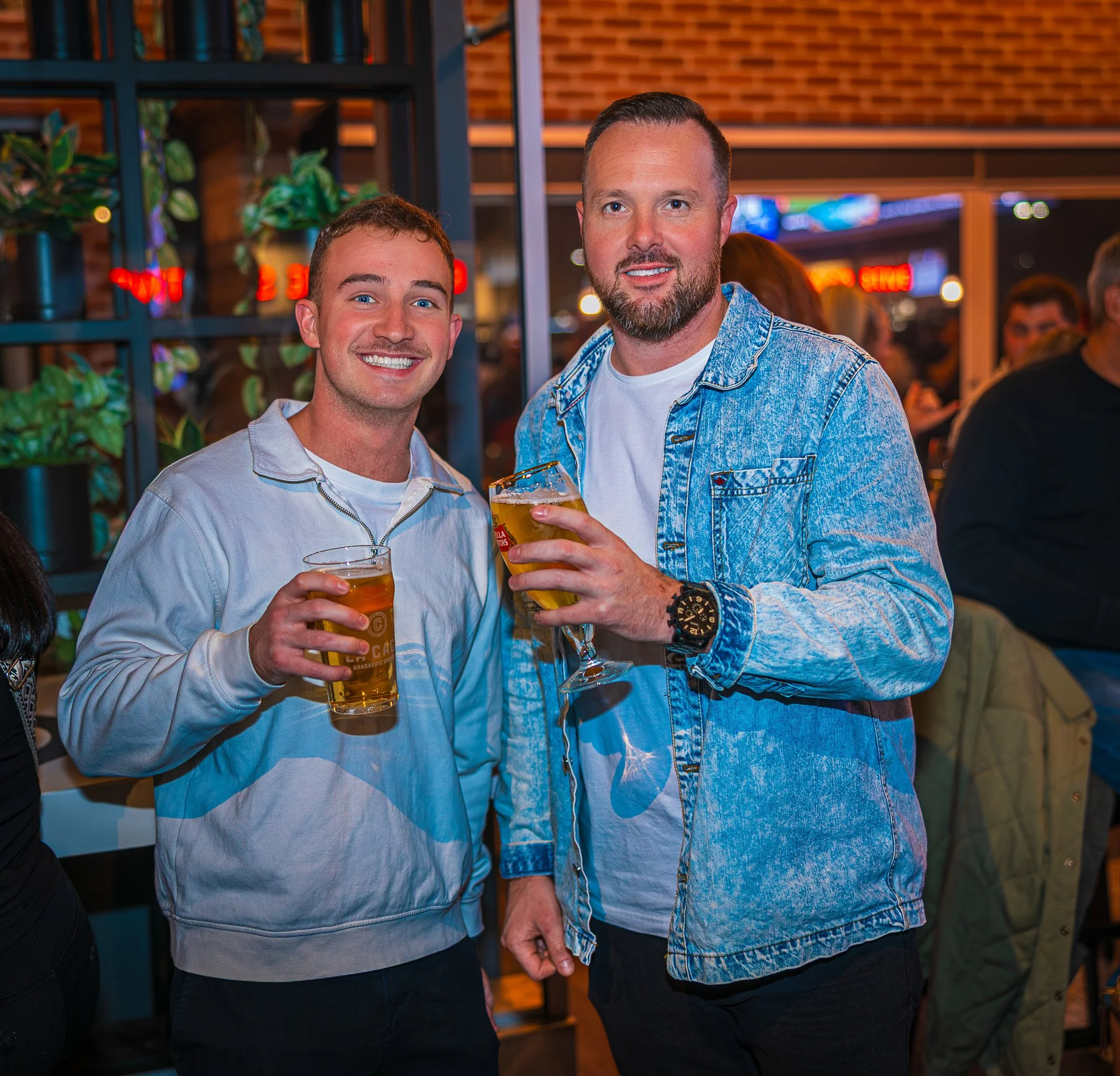 Two men smiling and holding drinks at a social gathering or bar.