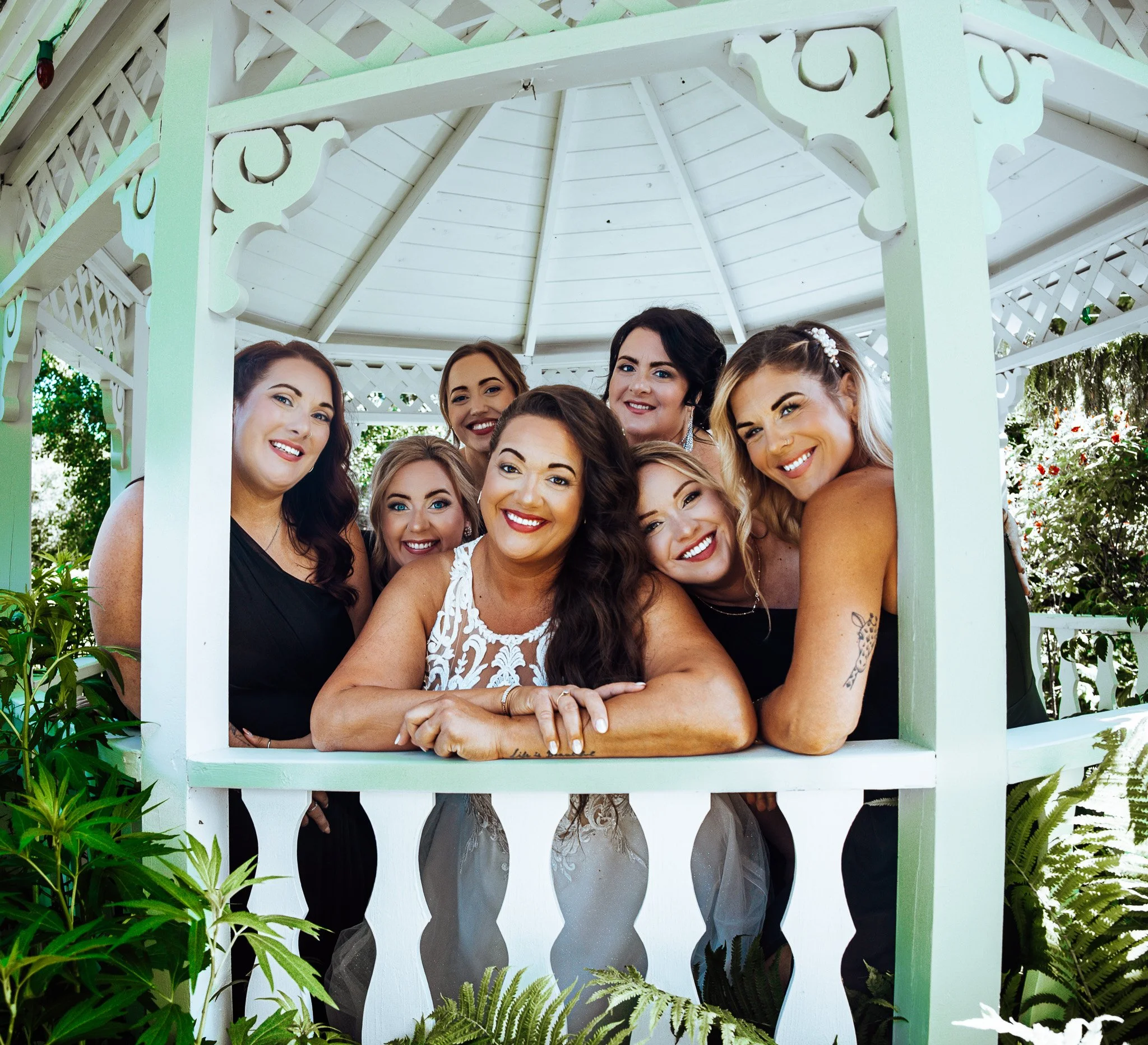 Group of women smiling and posing inside a white gazebo surrounded by greenery.