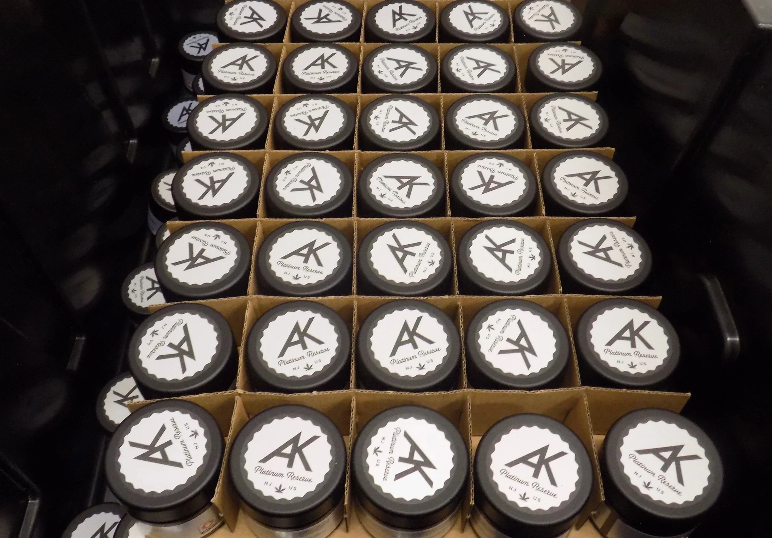Multiple jars of AK Platinum Reserve cannabis placed in cardboard trays, arranged in a grid pattern.