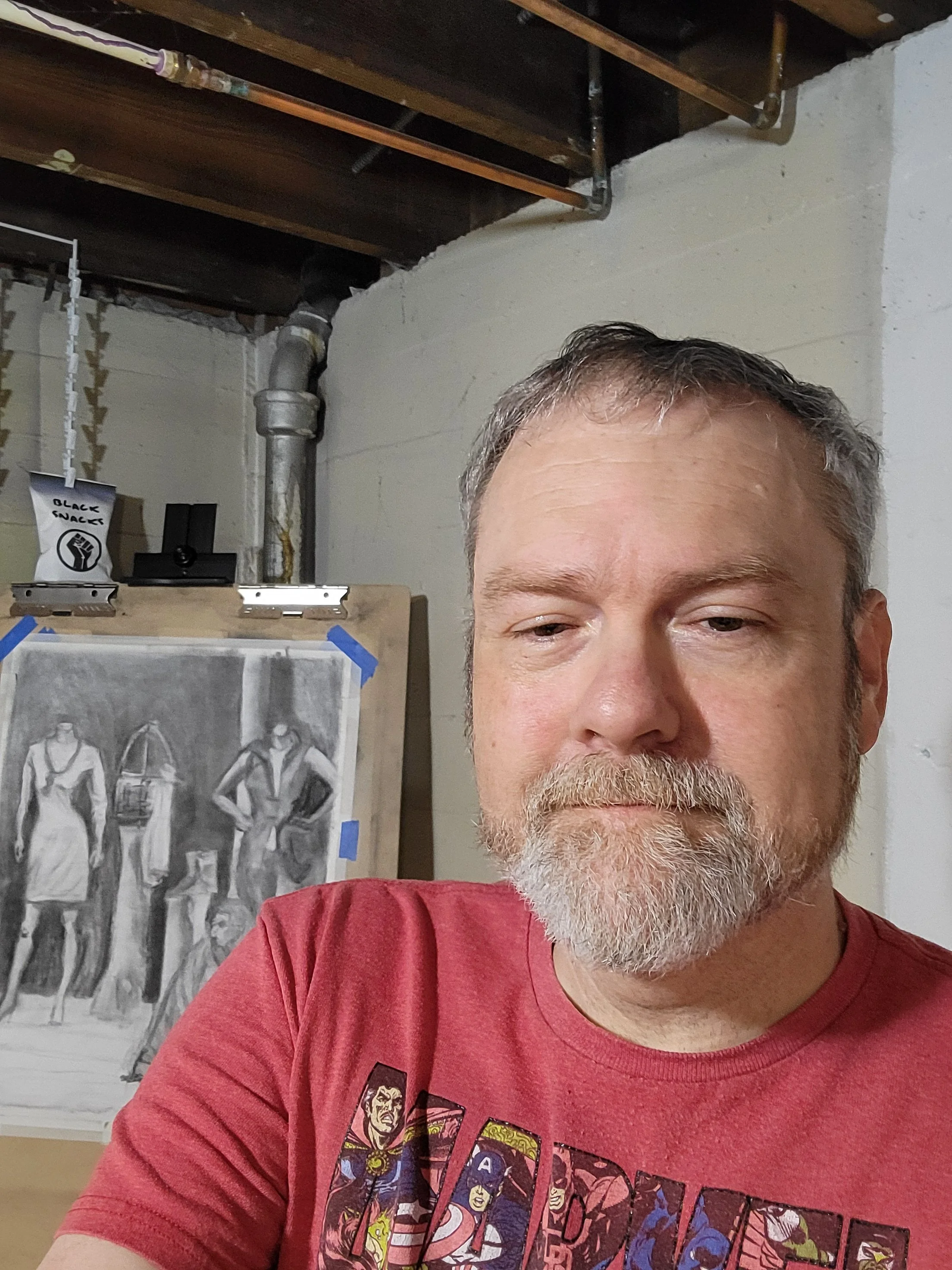 Mark Friday-Lewis in an art studio with a grayscale drawing of mannequins in the background.