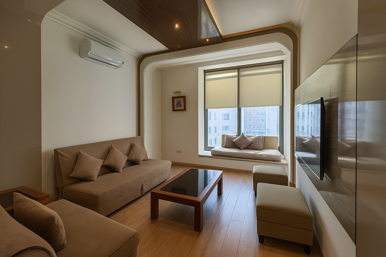 Living room with beige sofas, a coffee table, a window seat with cushions, and a wall-mounted TV, with a city view through large windows.