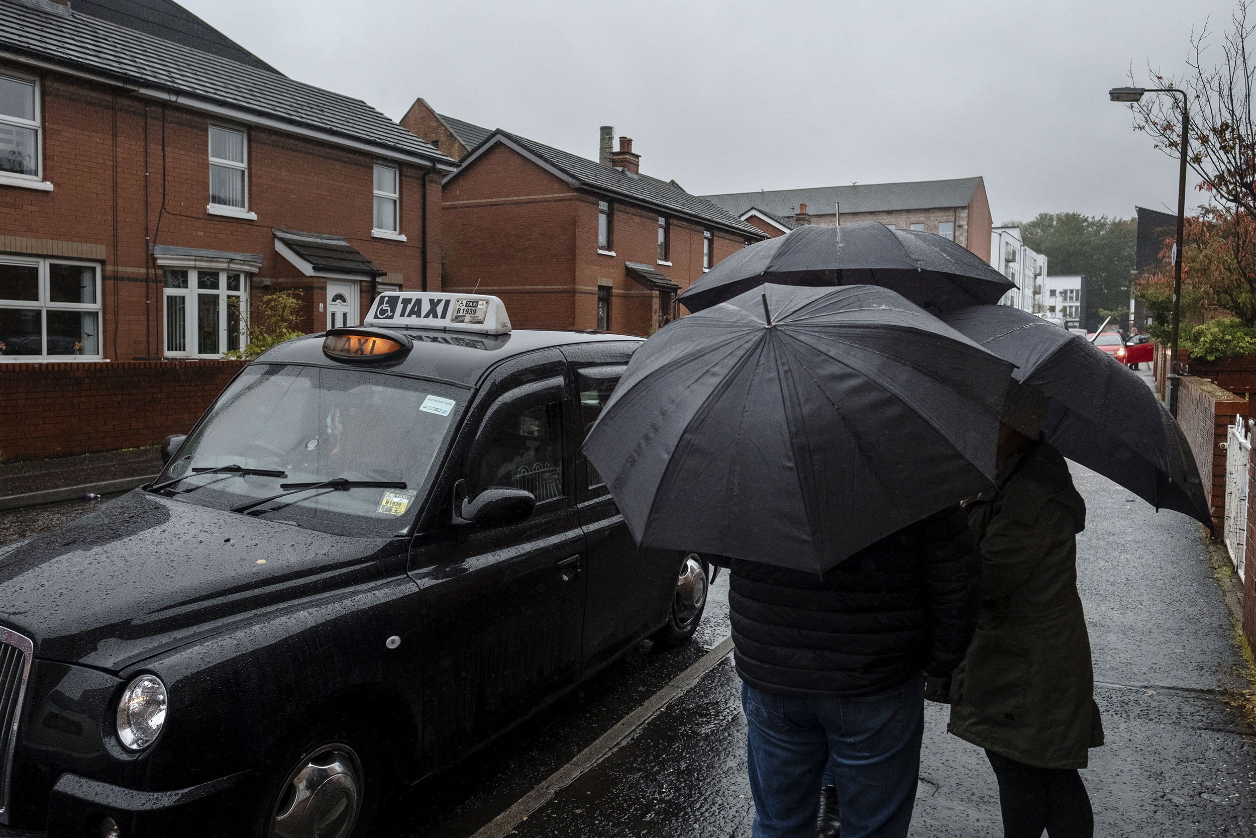Tourists shelter under umbrellas near the Bobby Sands mural, who was an IRA member that died on hunger strike while in prison. Belfast, Northern Ireland.