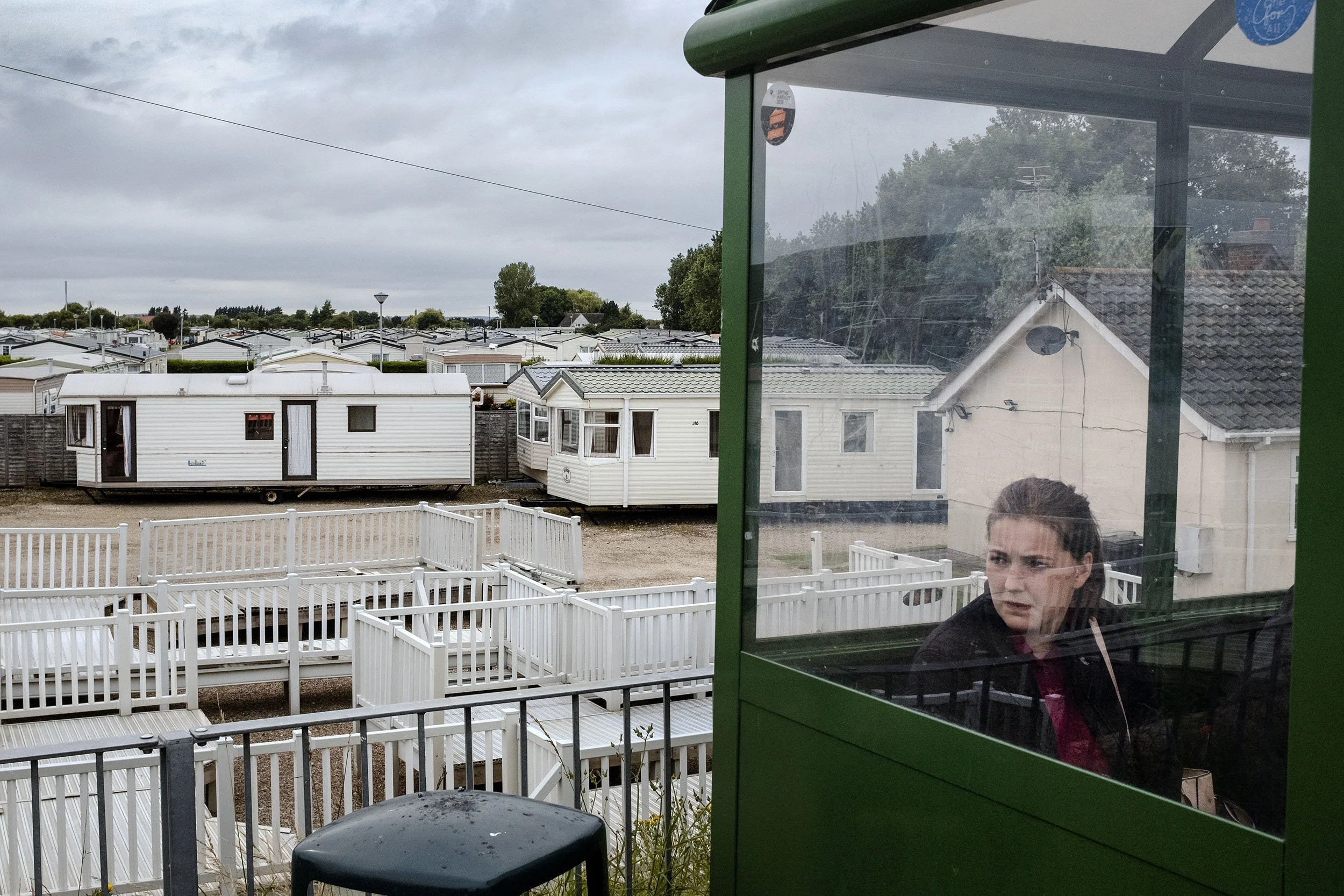 A lady waits for the bus at a bus shelter with a caravan park in the background. Skegness, England.