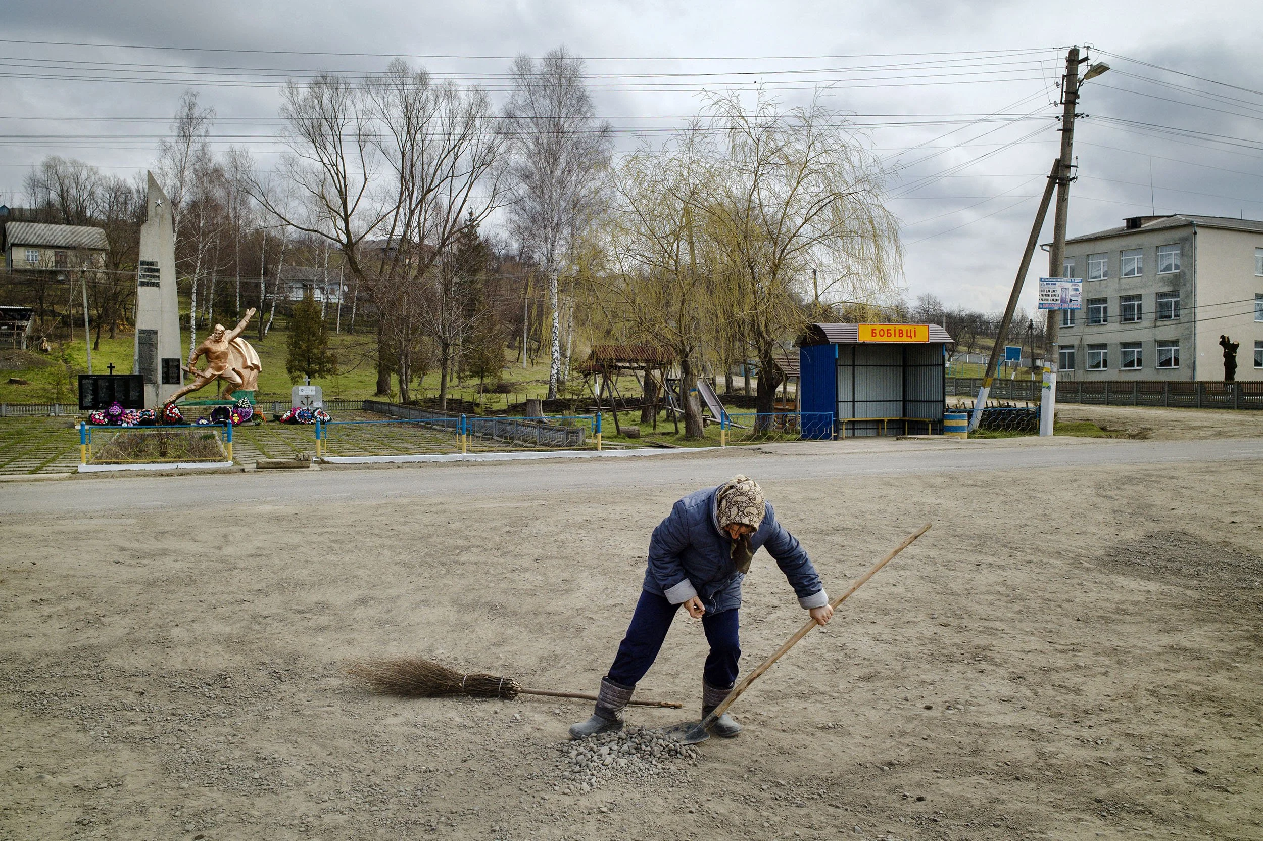 An elderly woman gathers stones alongside the road of the main square of Bobivtsi.