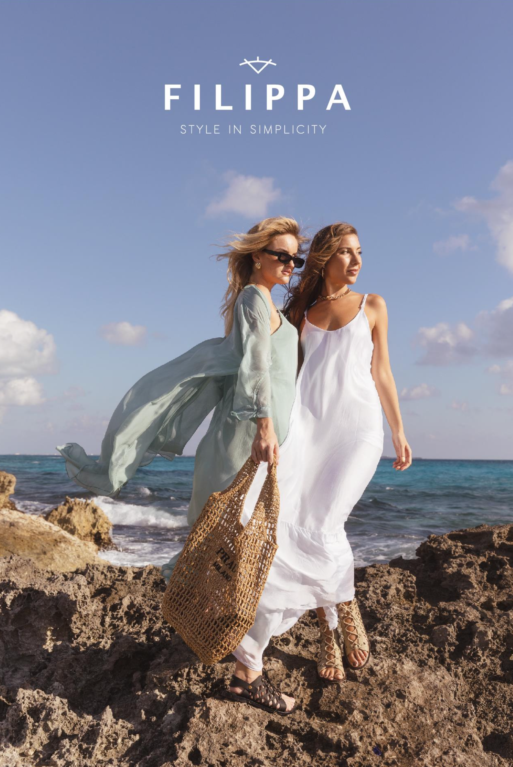 Two women in flowing dresses standing on rocks by the ocean with a blue sky overhead, one holding a woven bag, the other wearing sunglasses, promoting Fabippa fashion, with the tagline 'Style in Simplicity'.