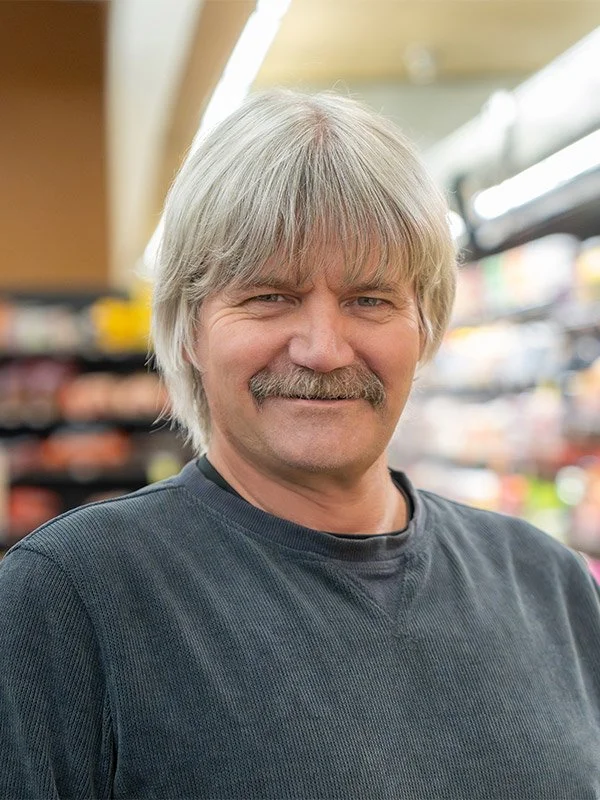 A middle-aged man with gray hair and a mustache smiling in a grocery store aisle.