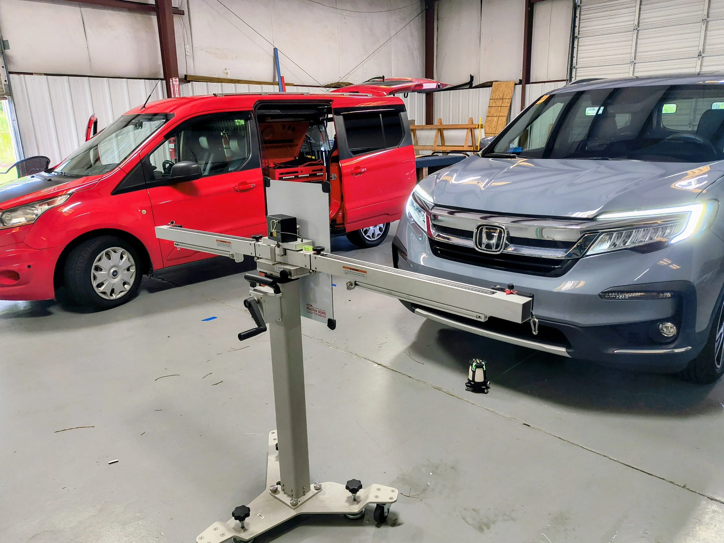 A red van and a gray Honda SUV parked inside a garage with a medical imaging machine in the foreground.