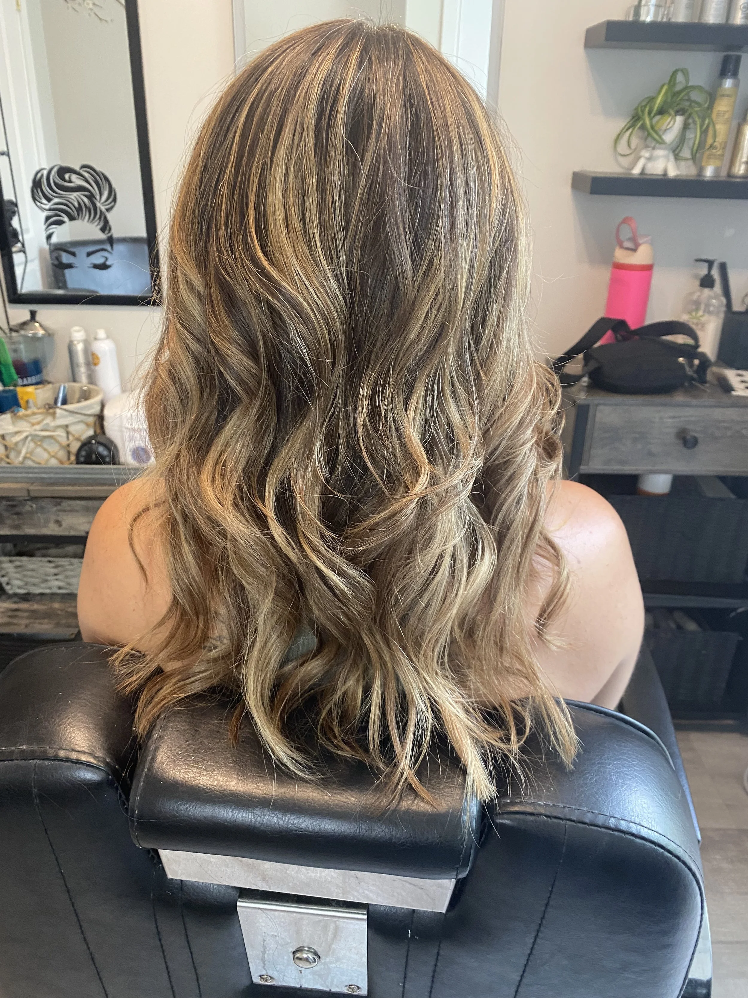 Back of a woman with wavy, shoulder-length blonde hair sitting in a salon chair.