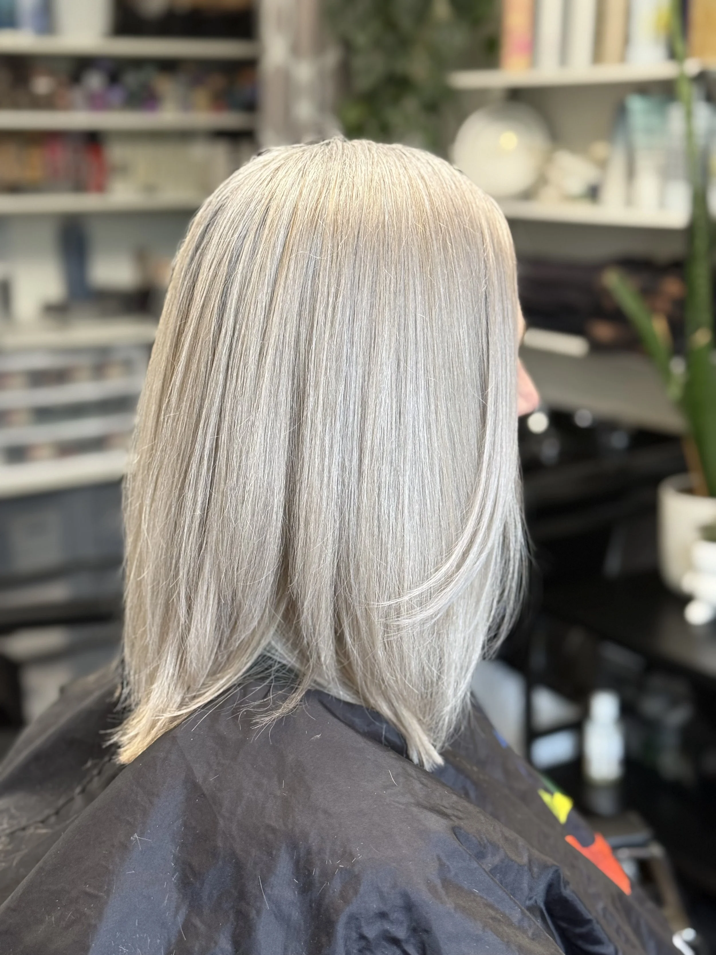 Side view of a woman with shoulder-length, straight, silver-colored hair in a salon setting.