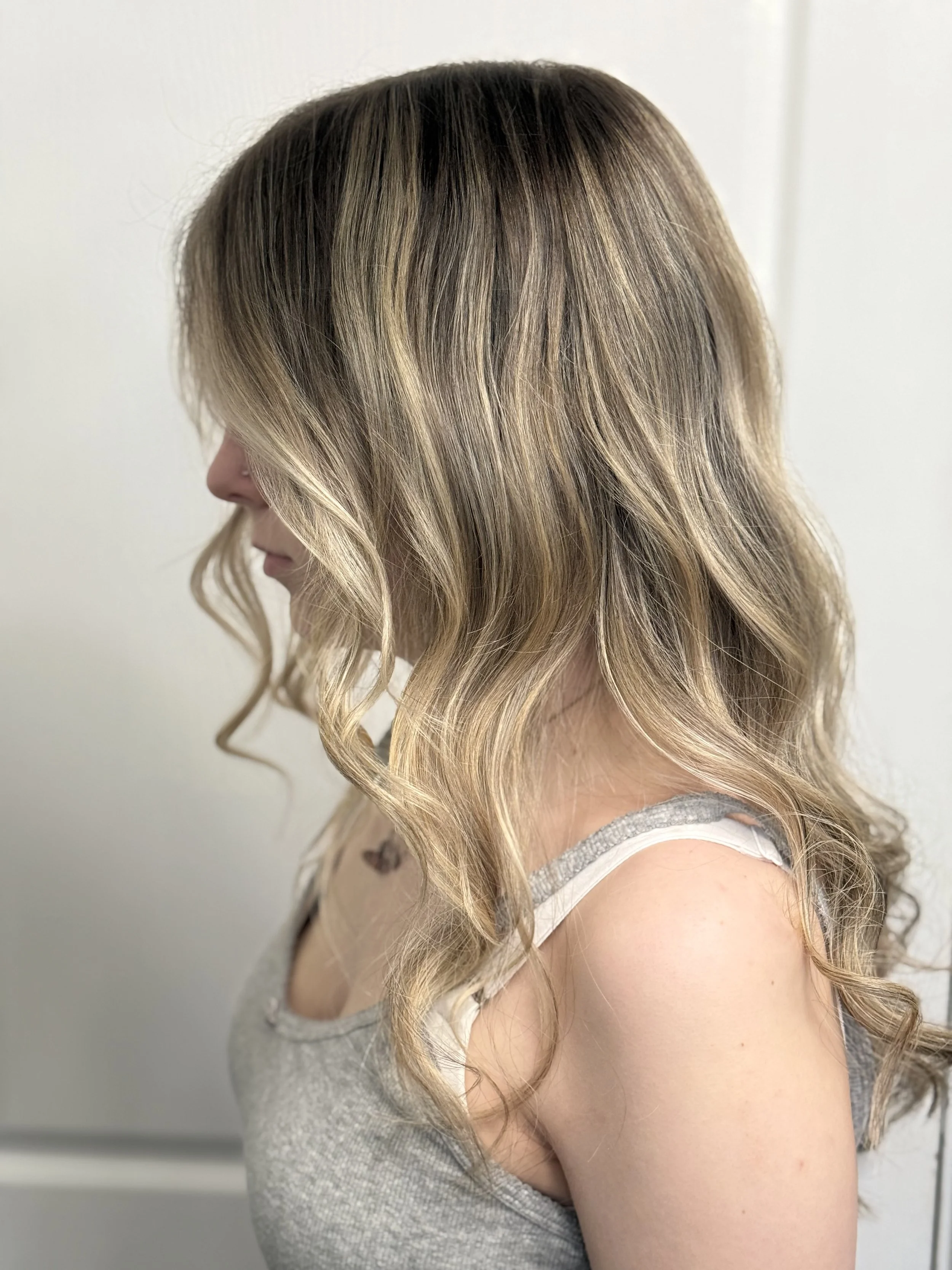 Side view of a woman with long, wavy, blonde hair against a plain background.