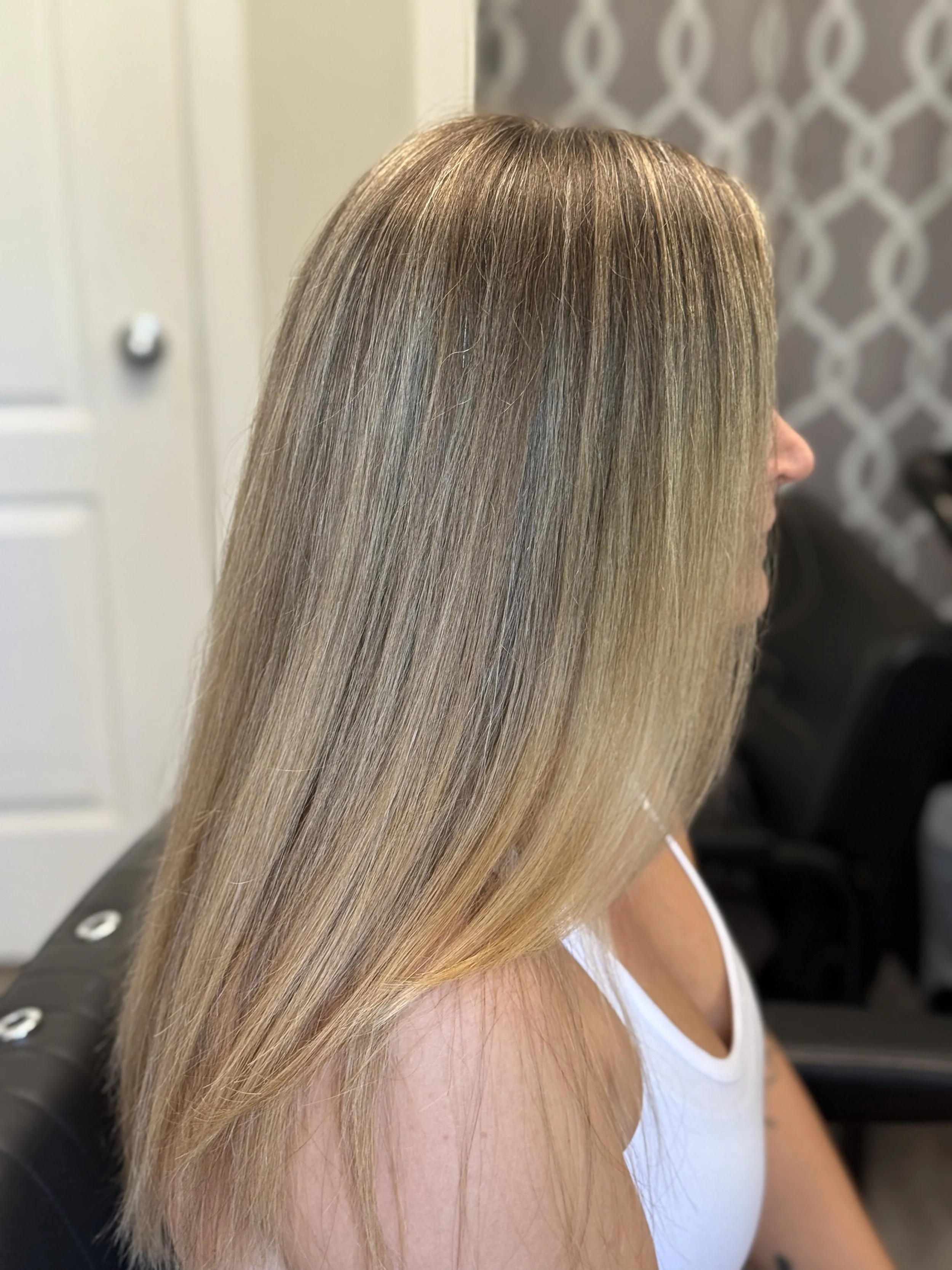 Side view of a woman with long, straight, blonde hair sitting in a salon chair.