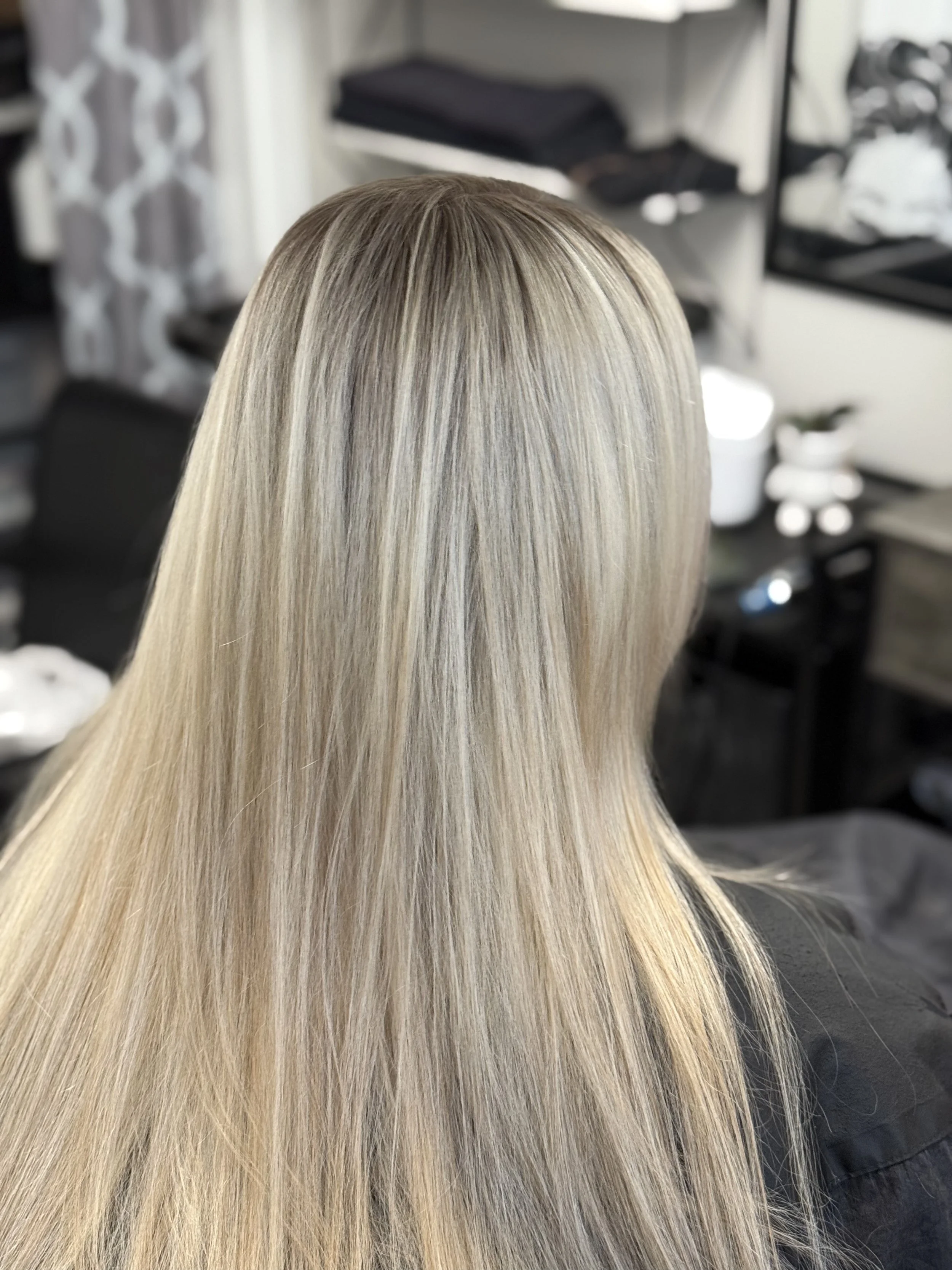 Back view of a woman with long, straight, blonde hair in a salon or styling studio.