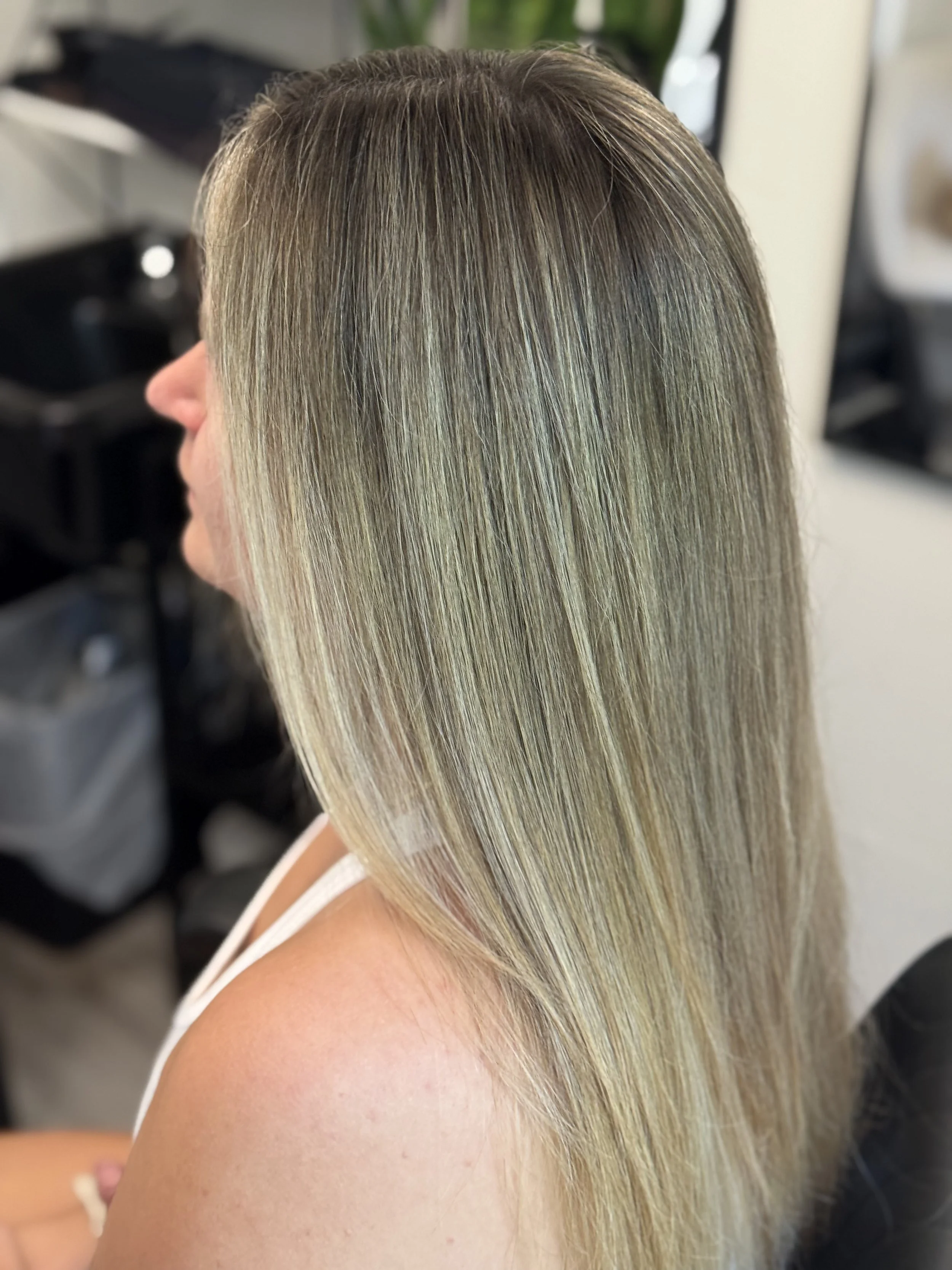 Side view of a woman with long, straight blonde hair in a hair salon.