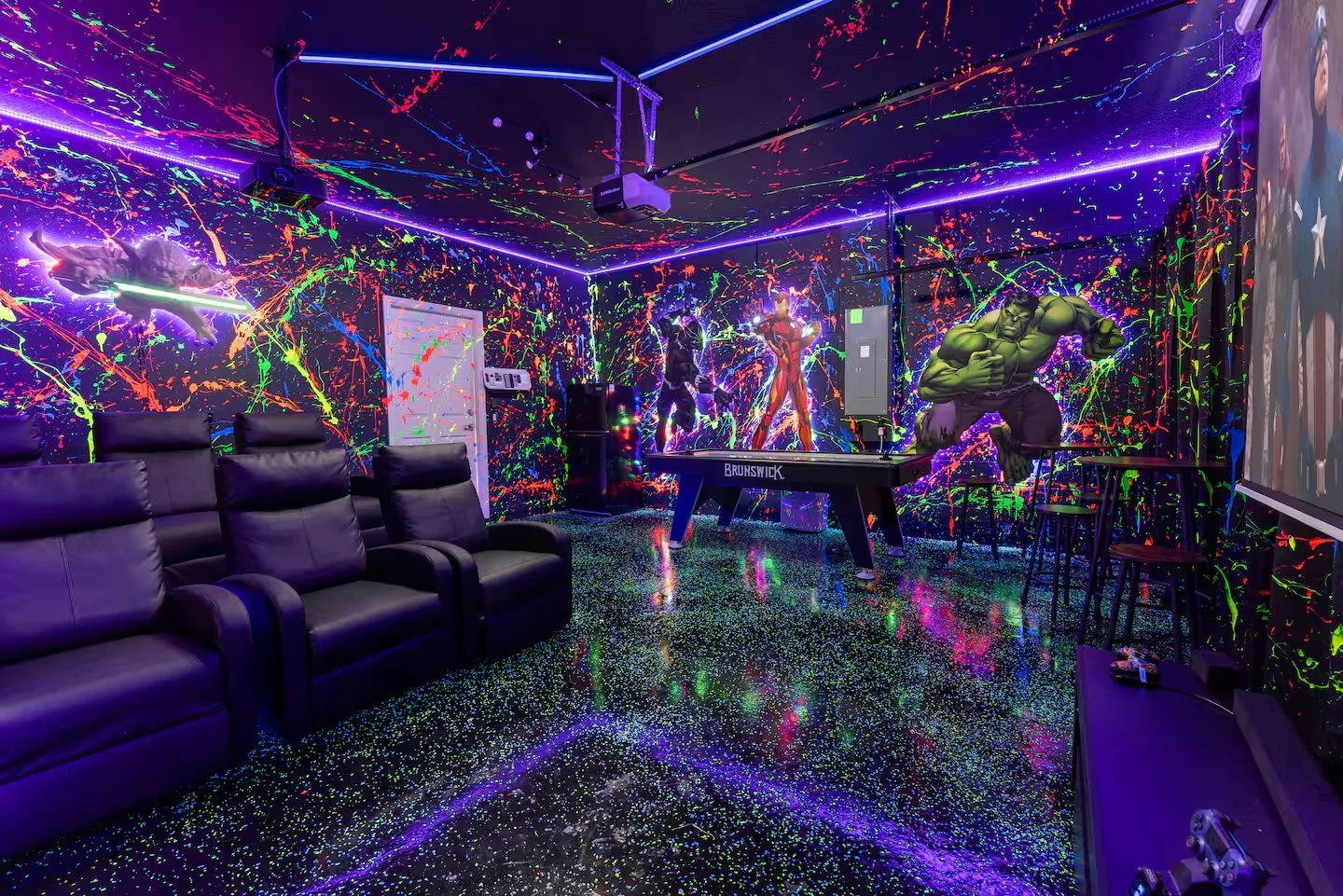 A neon-lit game room with splatter paint walls featuring Marvel superheroes like The Hulk and Iron Man. Themed room in vacation rental in Kissimmee florida on storey lake